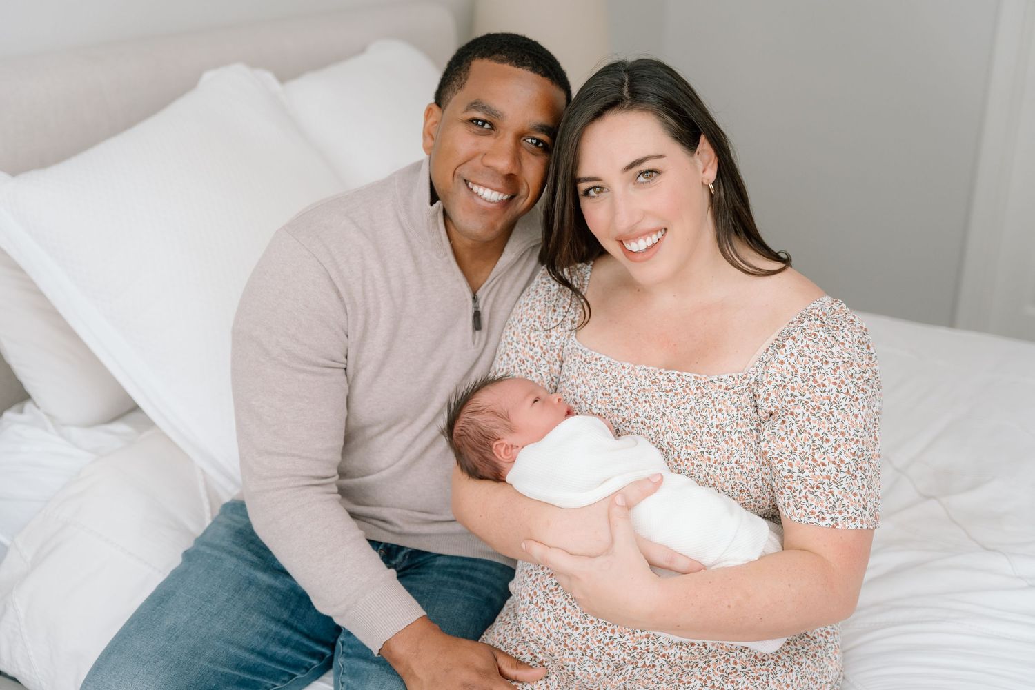 Newborn photography session featuring parents and baby on white bedding.