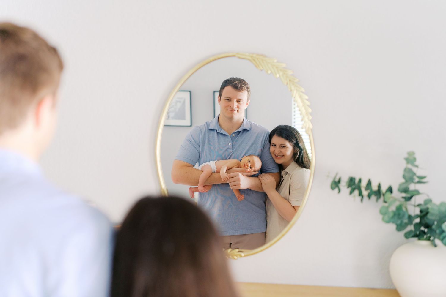 Modern family photoshoot with minimalist decor and a round gold mirror on white walls.