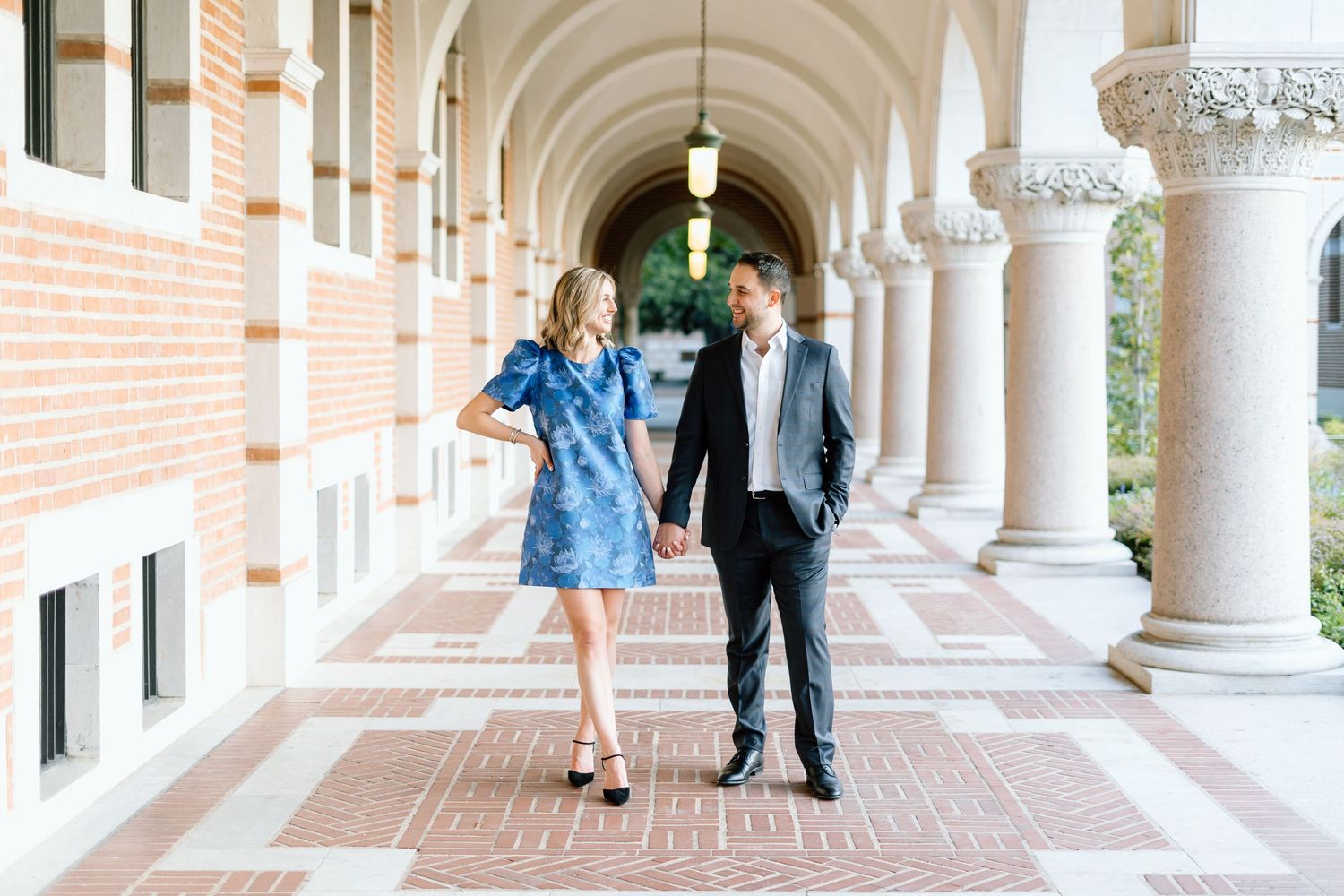 People walking through elegant arched colonnade with brick and white columns.