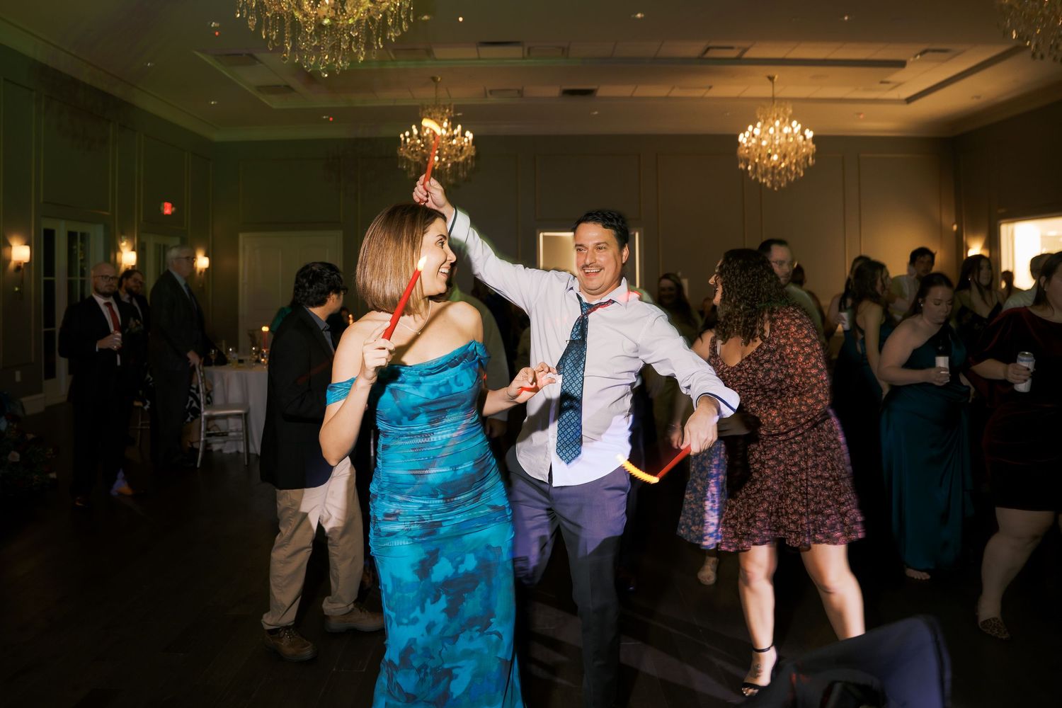 Wedding guests dancing enthusiastically under chandeliers at an elegant indoor reception.