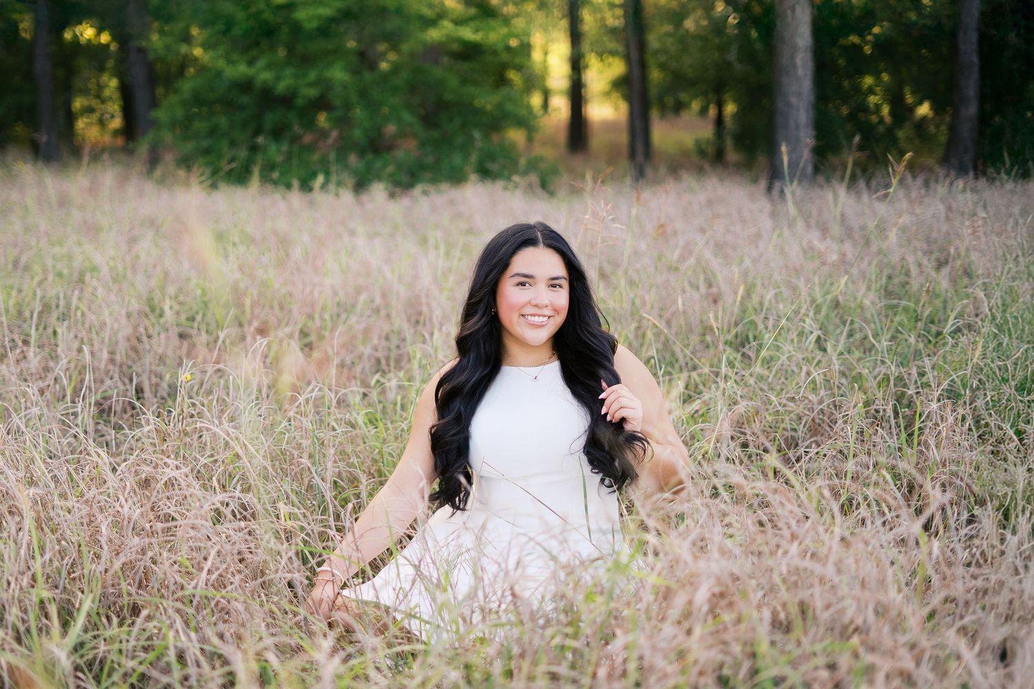 Woman in white dress poses gracefully in a golden field during sunset.
