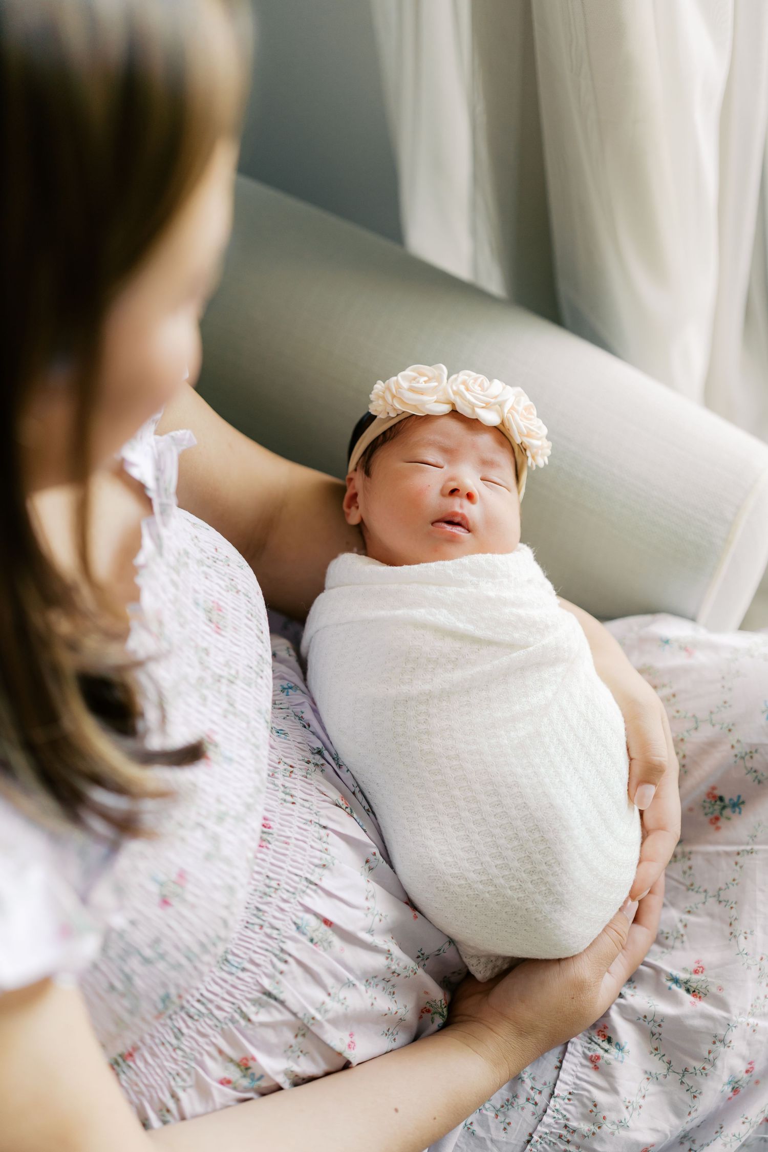 Sleeping newborn wrapped in white swaddle with delicate floral headband.
