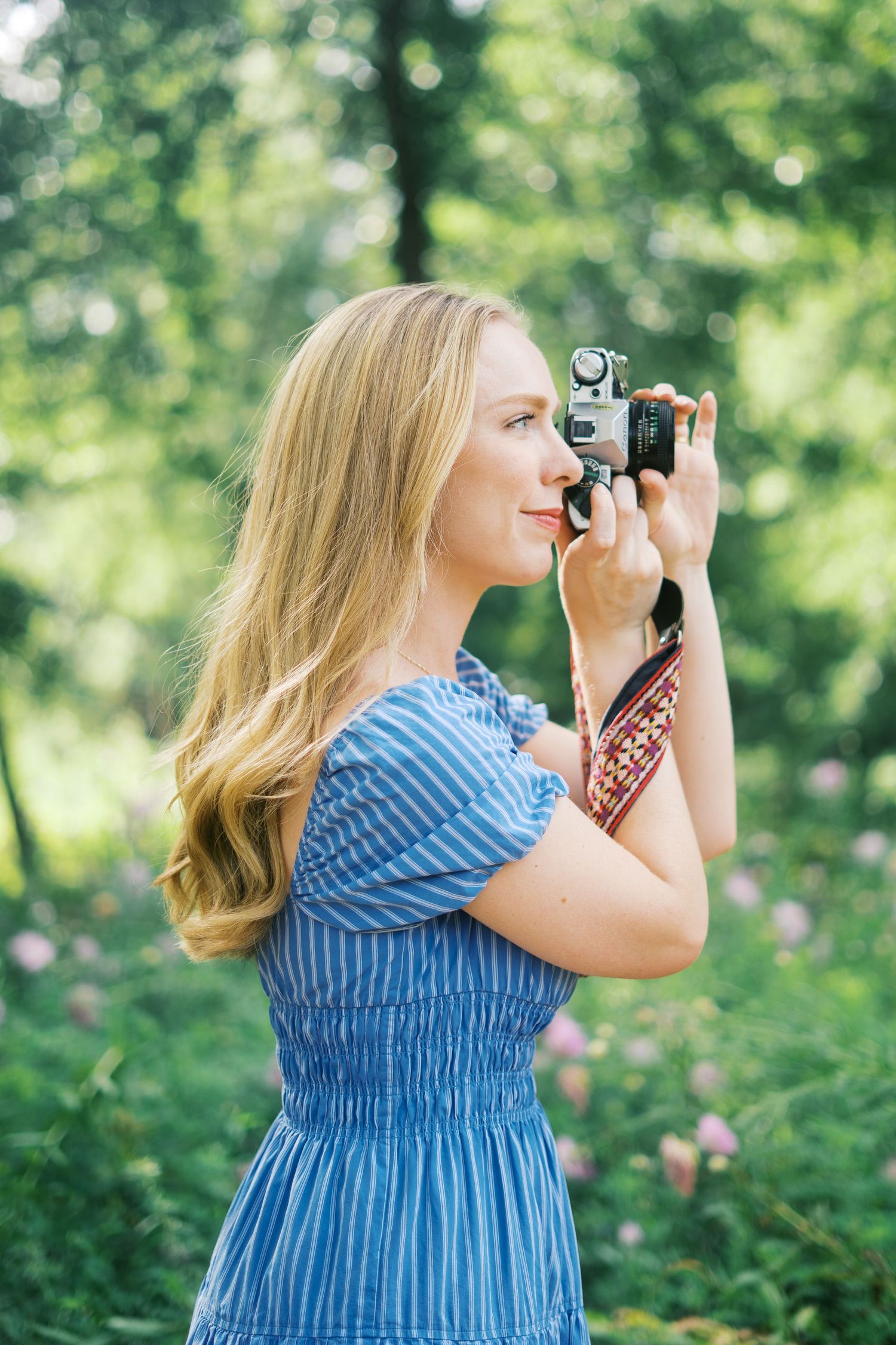 Photographer in blue striped dress taking pictures outdoors in a garden setting.