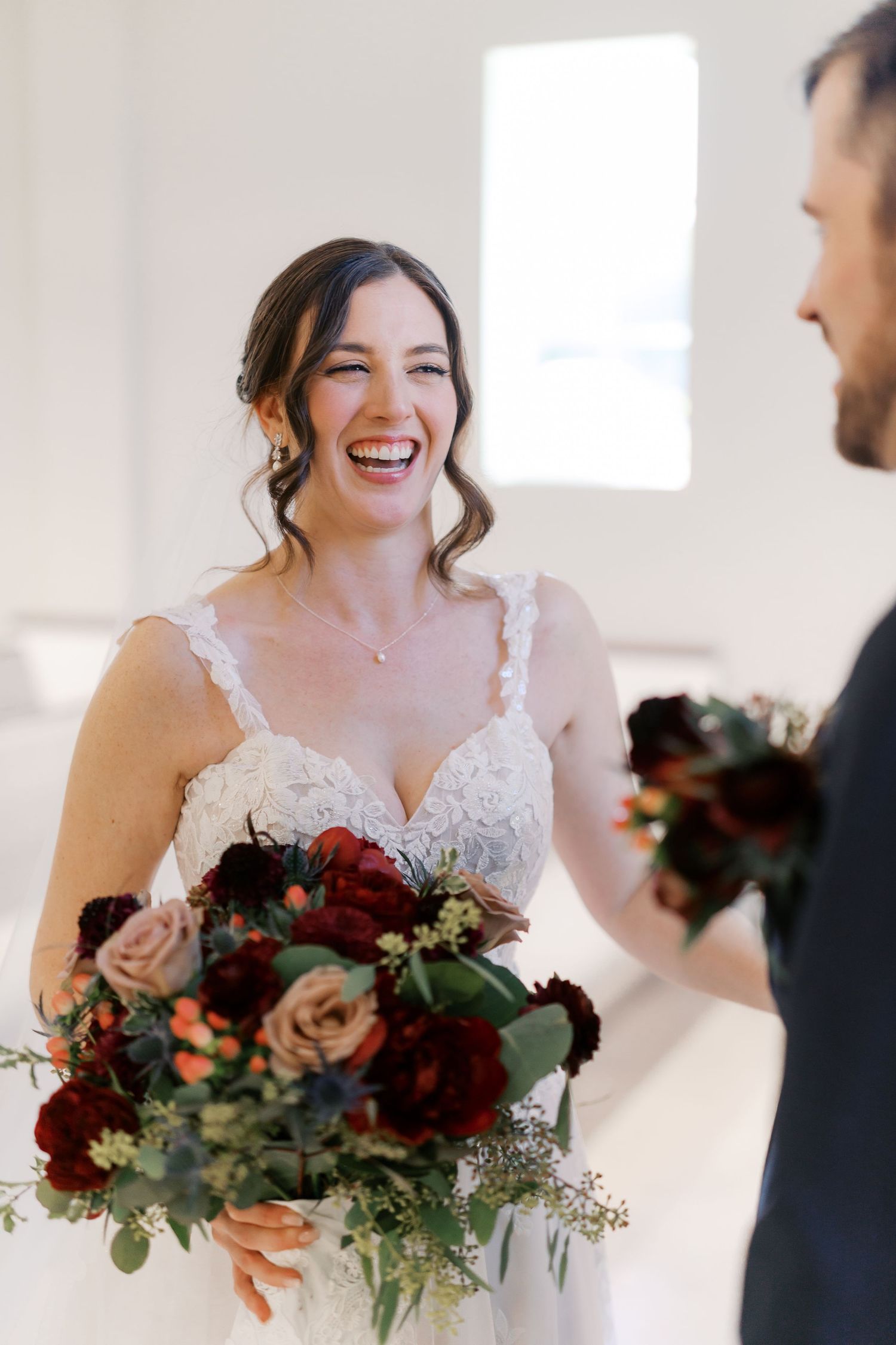 A couple shares laughter during their wedding first look with burgundy floral bouquet.