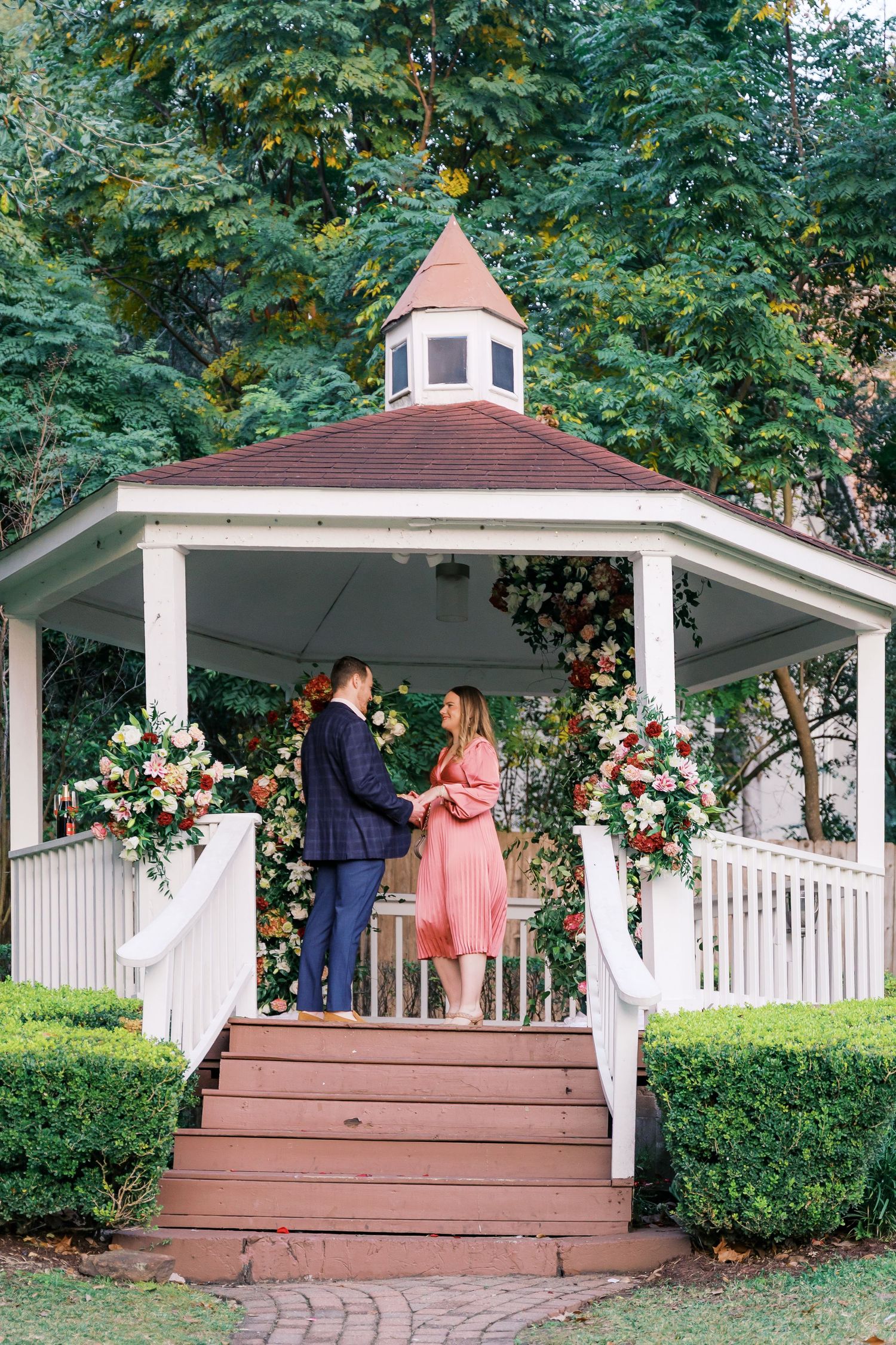 A couple shares a special moment on a gazebo deck decorated with floral arrangements and white railings.
