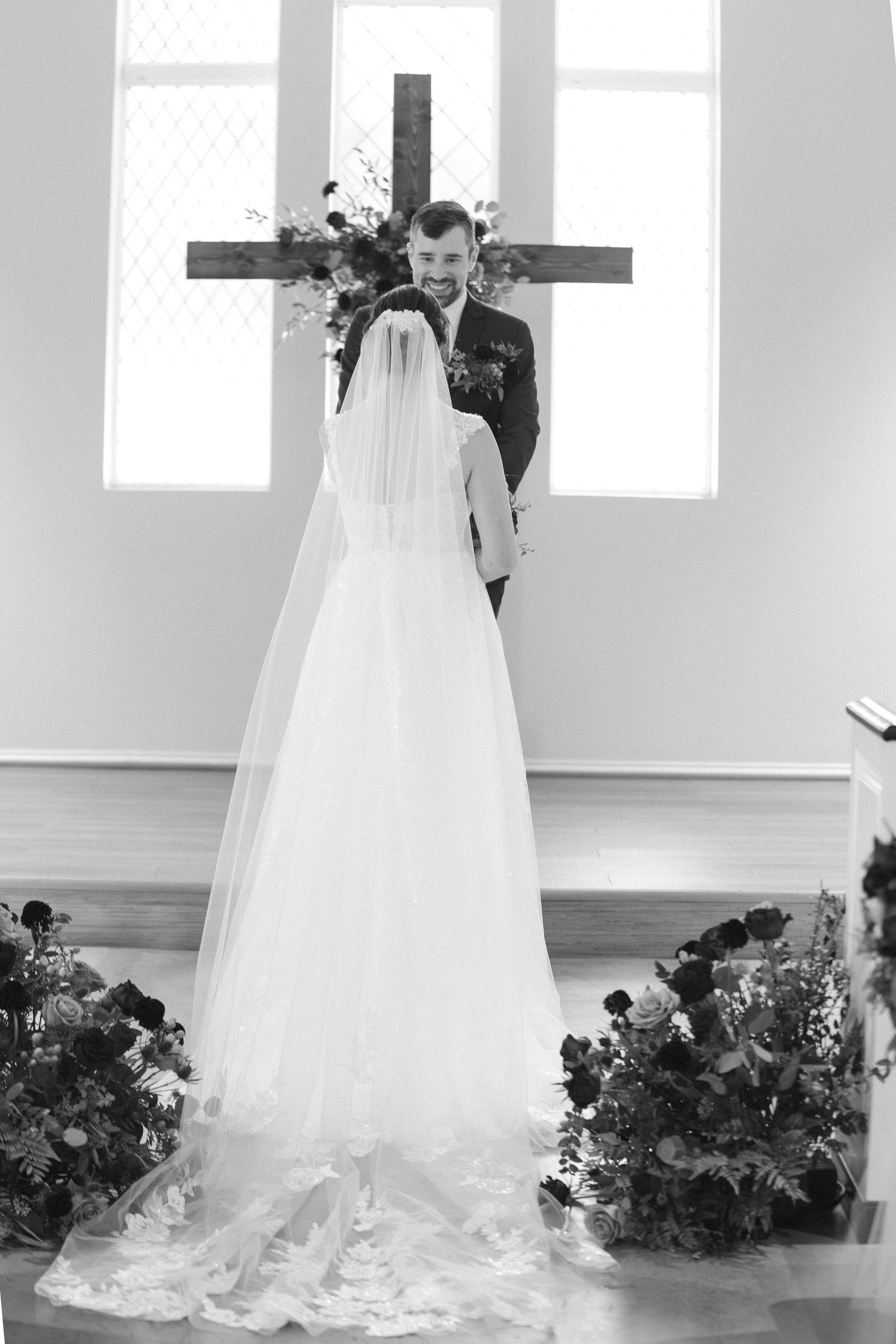A wedding couple stands together in a sunlit church with elegant floral decorations.