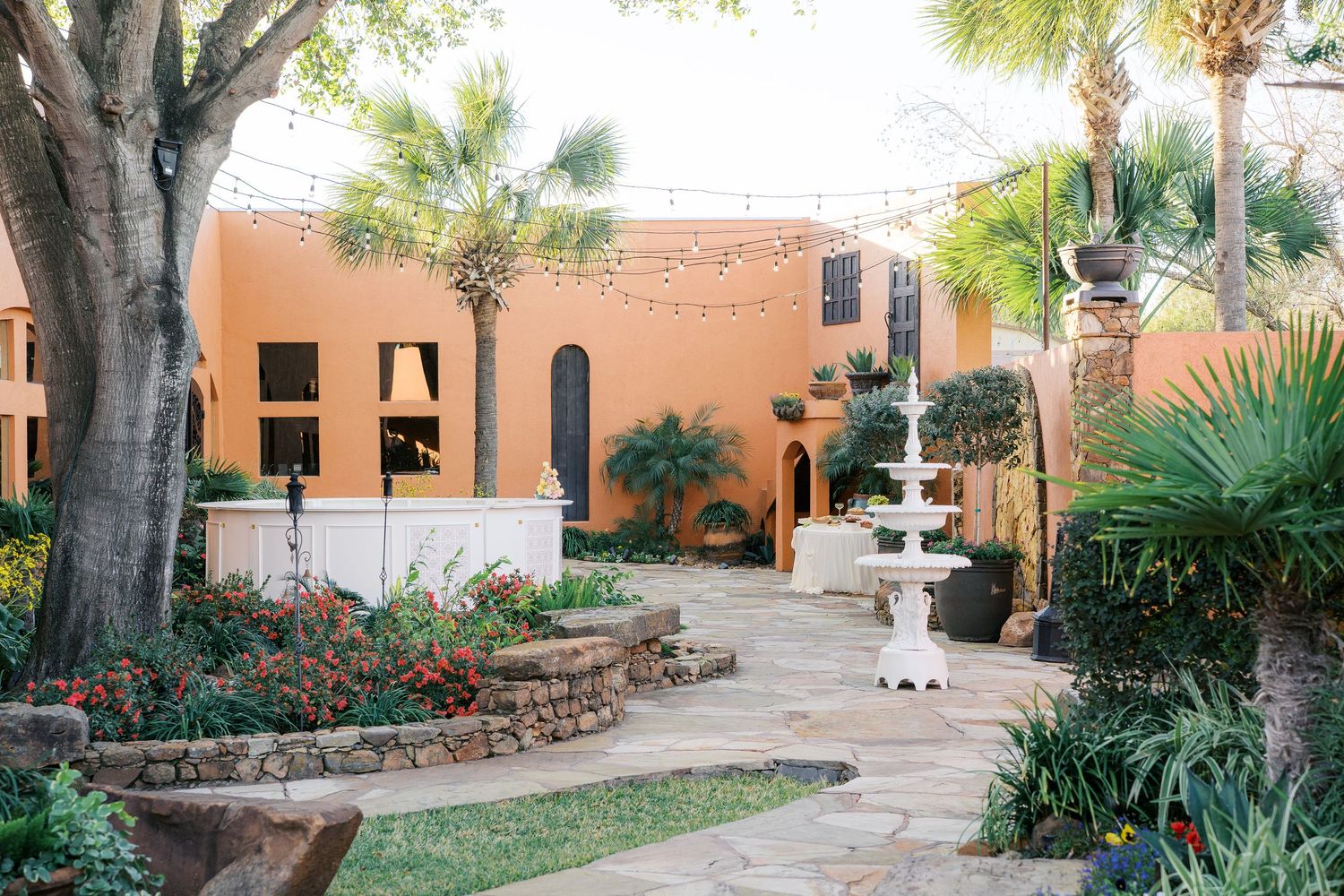 Elegant outdoor courtyard with a tiered fountain, lush gardens, and warm terracotta building at a wedding venue.