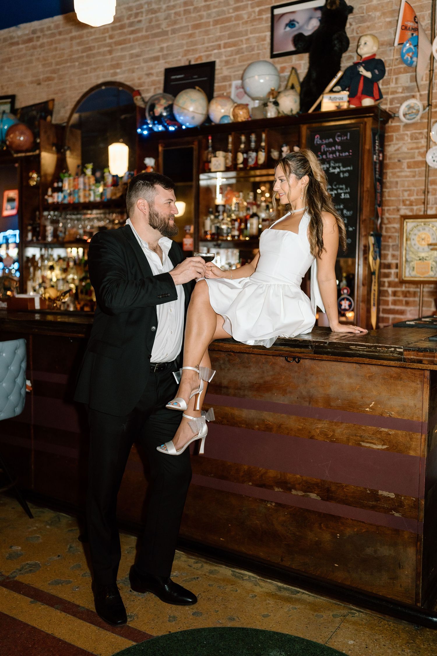 Couple shares romantic moment against rustic bar backdrop with exposed brick and vintage decor.