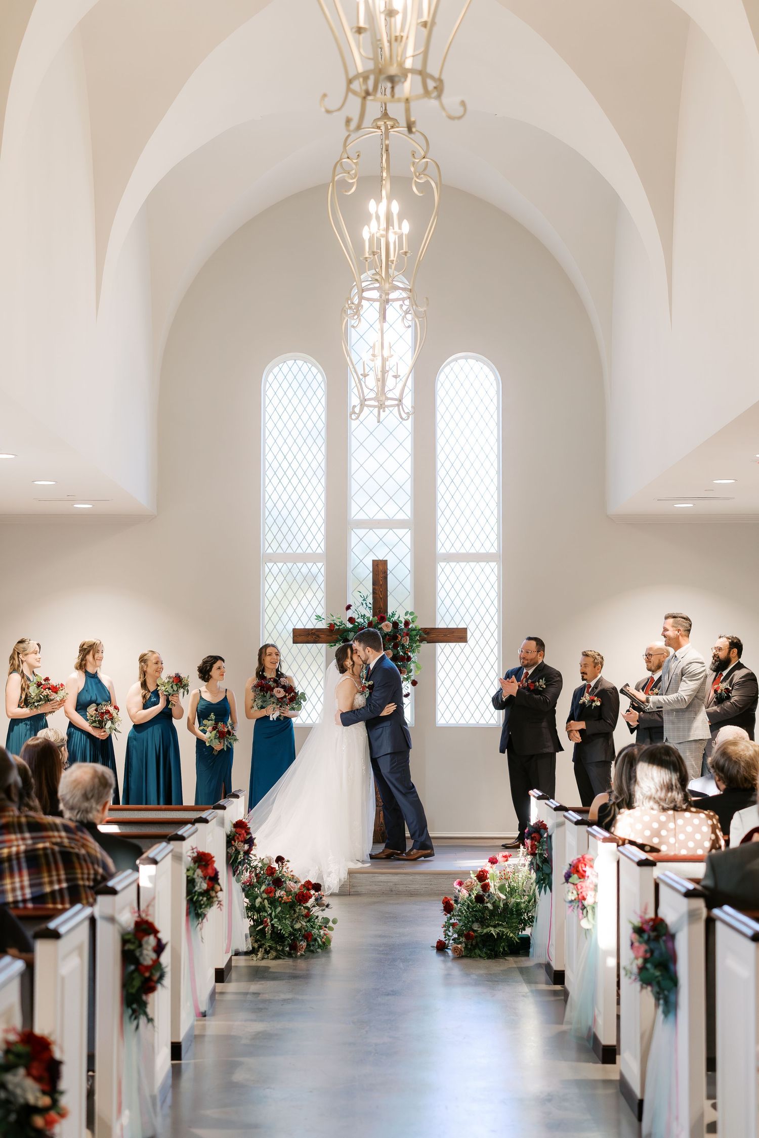 Elegant white chapel interior with arched ceilings and crystal chandeliers during wedding ceremony.