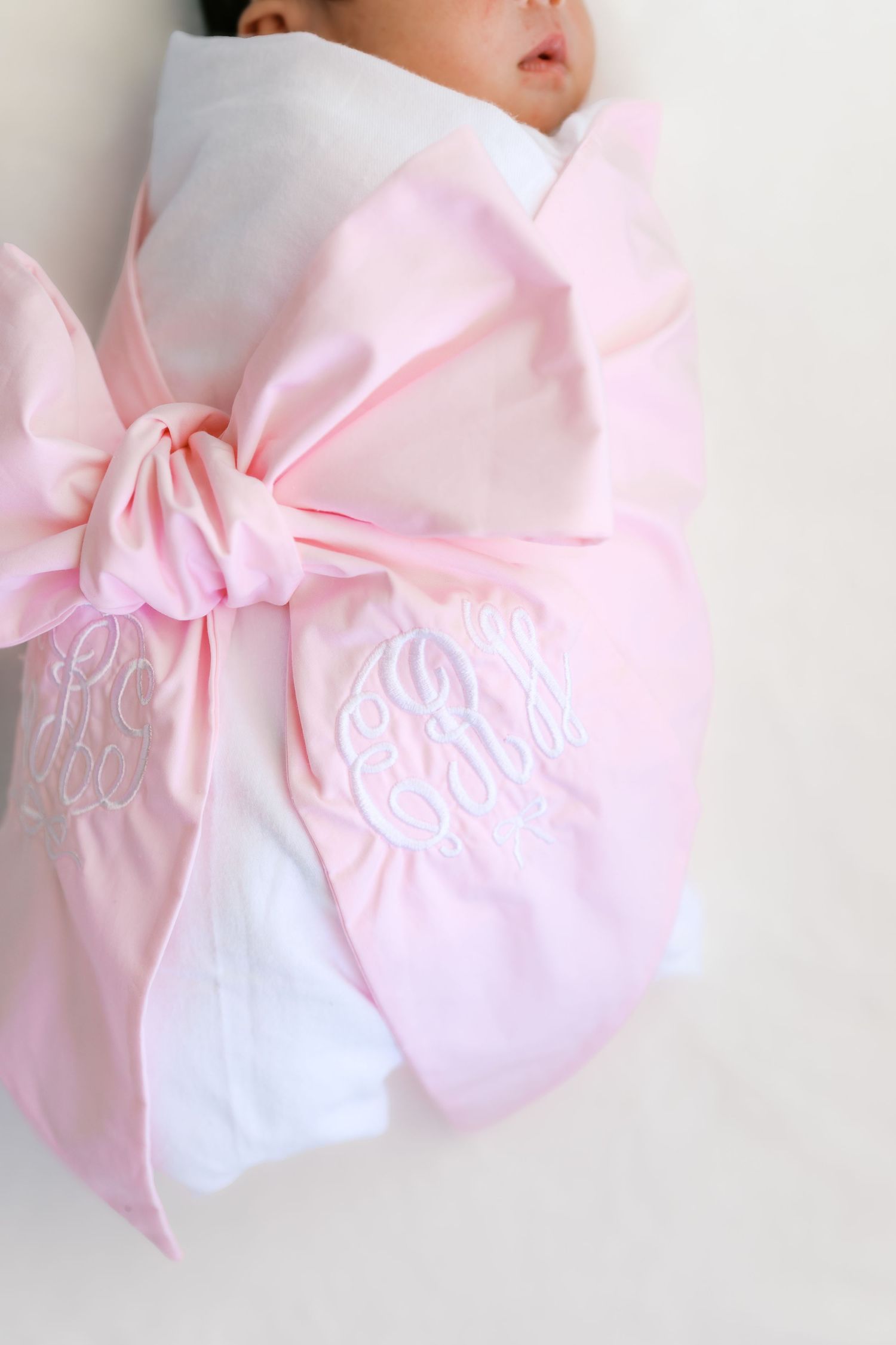 Close-up of monogrammed pink bow swaddle wrap with white embroidery detail.