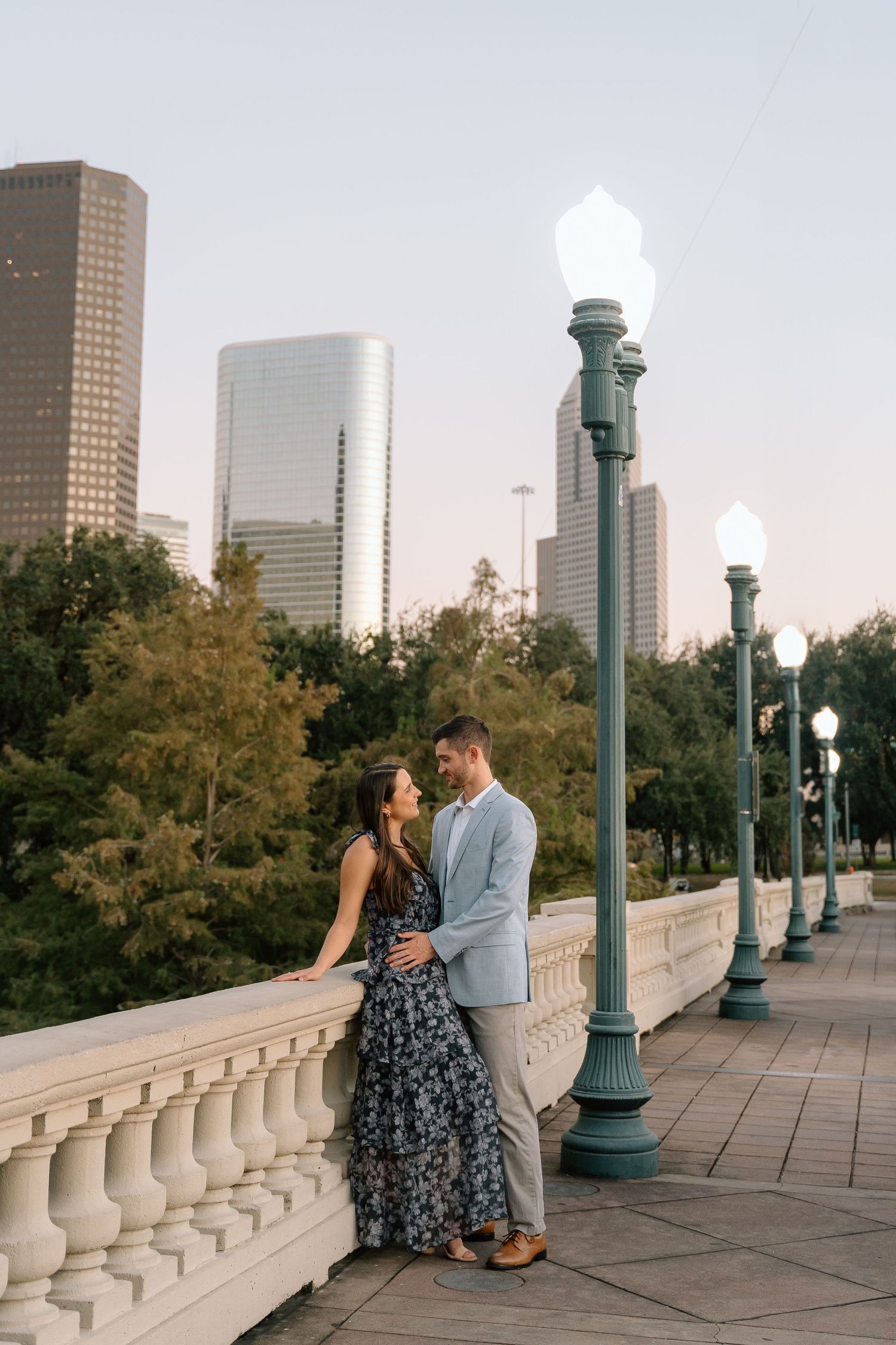 Romantic sequence on stone balcony with city skyline and vintage lampposts in background.