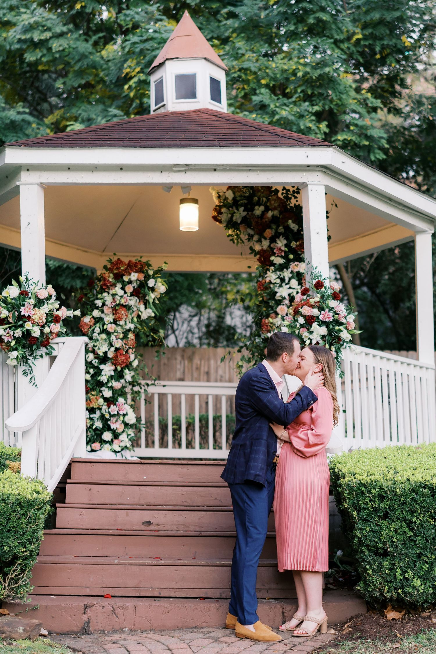 Romantic proposal scene in a decorated white gazebo with floral arrangements.