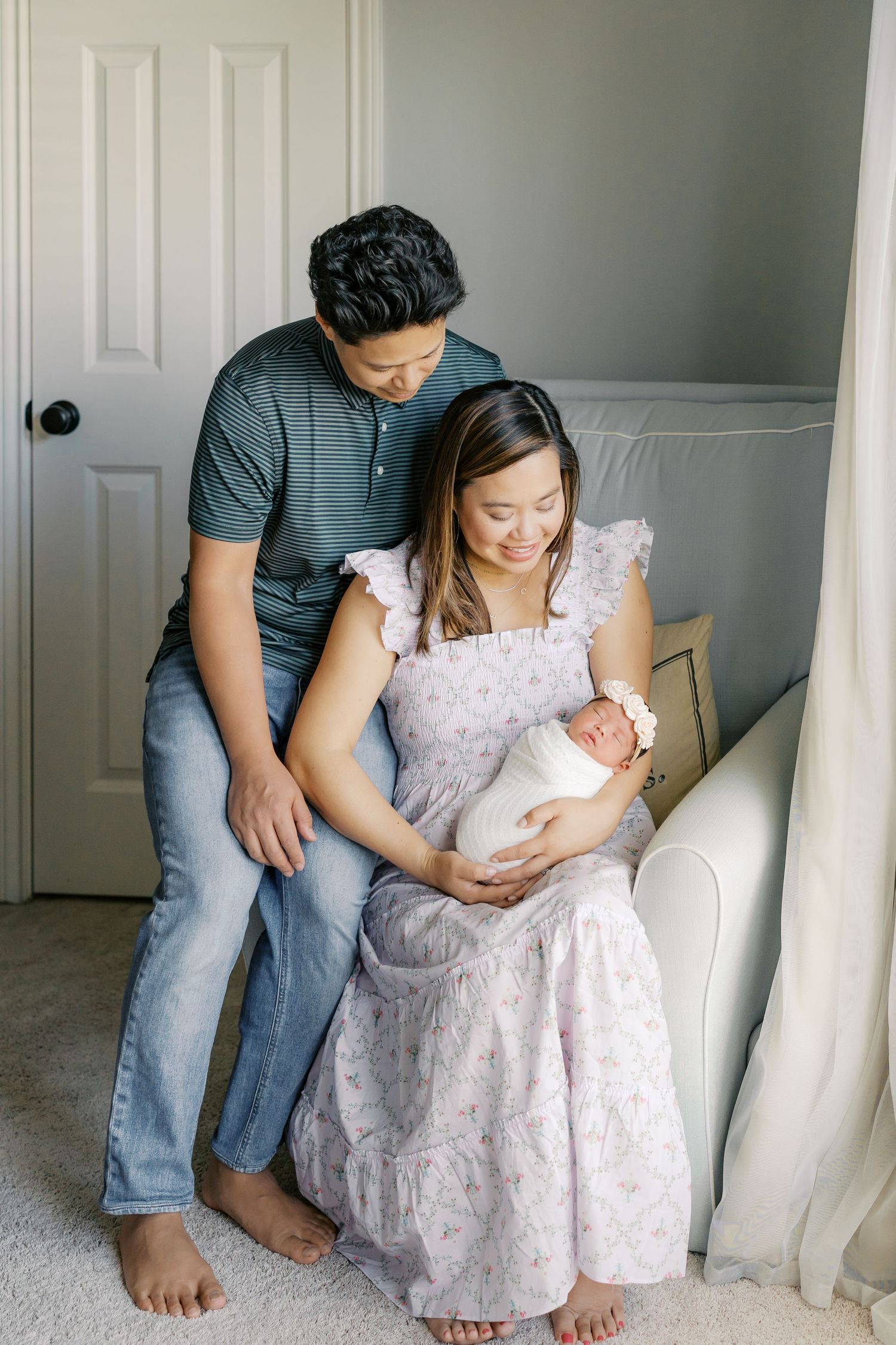 Family portrait showing parents sitting together with their newborn baby in a bright room.