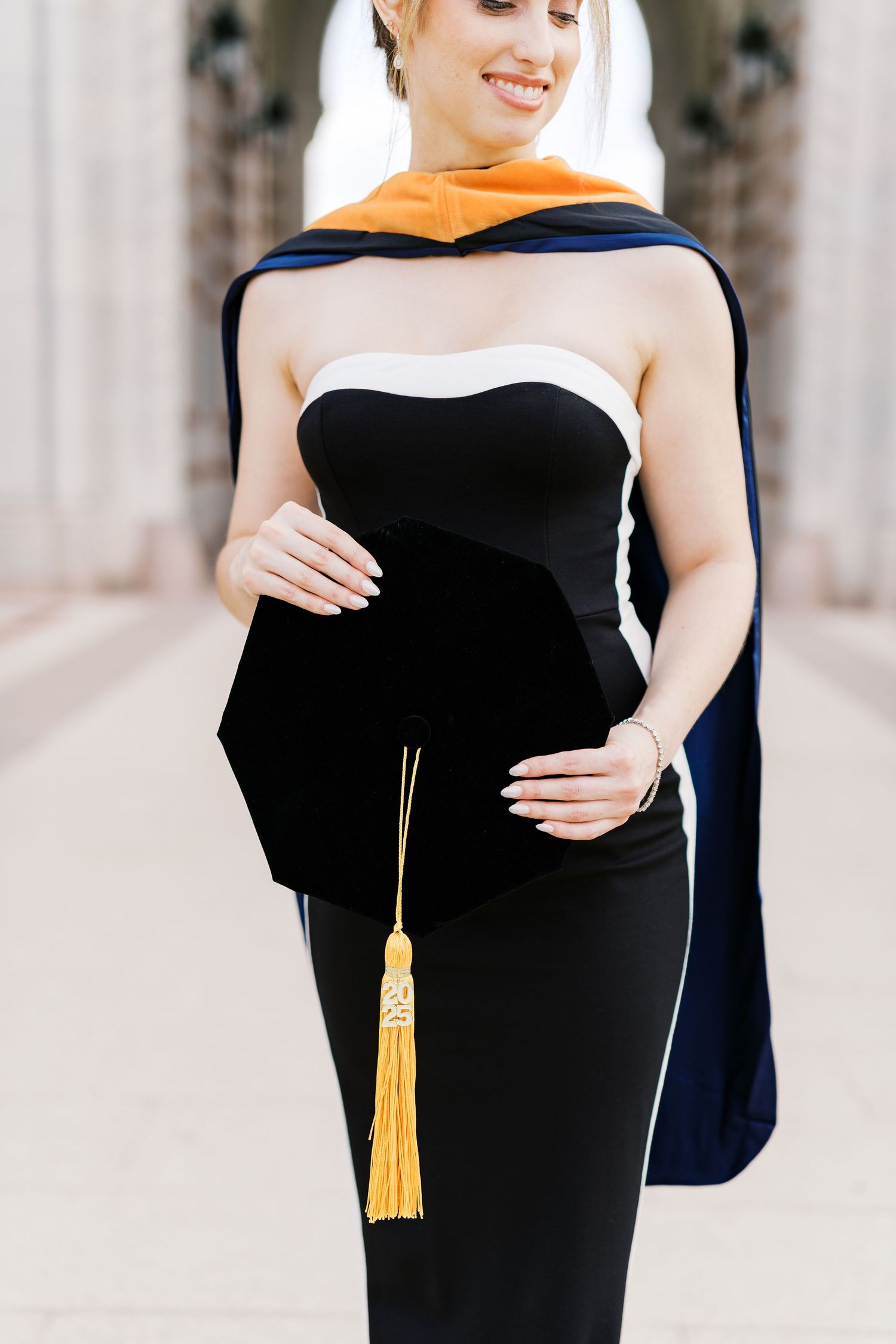 A formal graduation photoshoot featuring a black dress with gold tassel details.