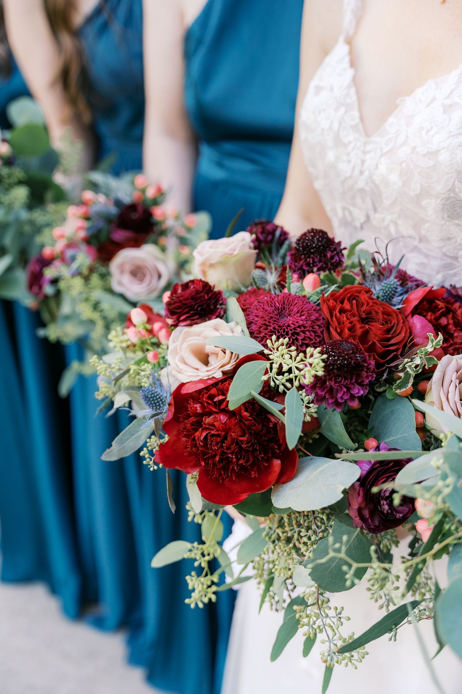 Close-up of burgundy and blush wedding bouquet with roses and greenery.