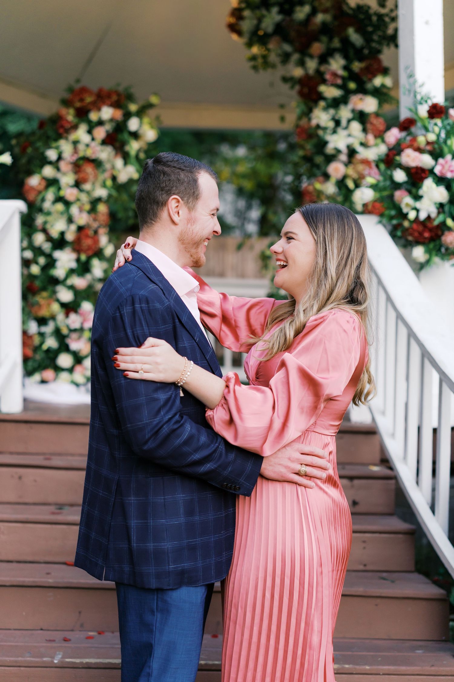 A couple in formal wear shares loving moments on a porch decorated with floral arrangements.