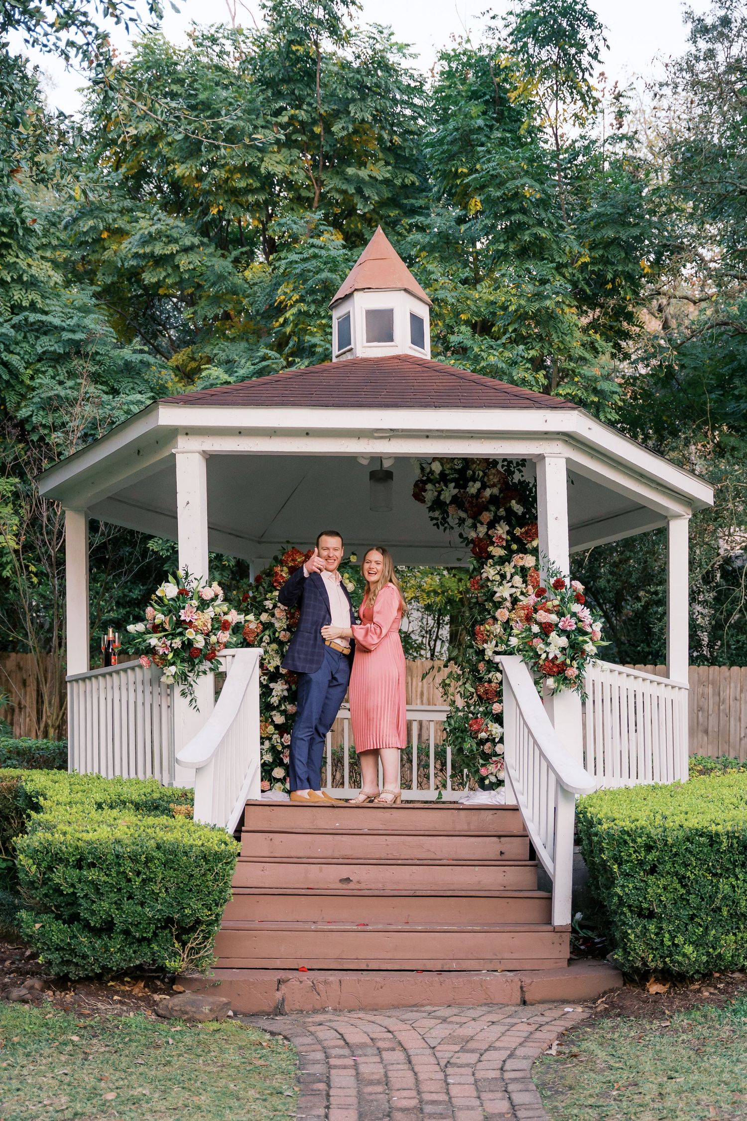 A beautiful garden gazebo moment with floral decorations and brick pathway leading to wooden steps.