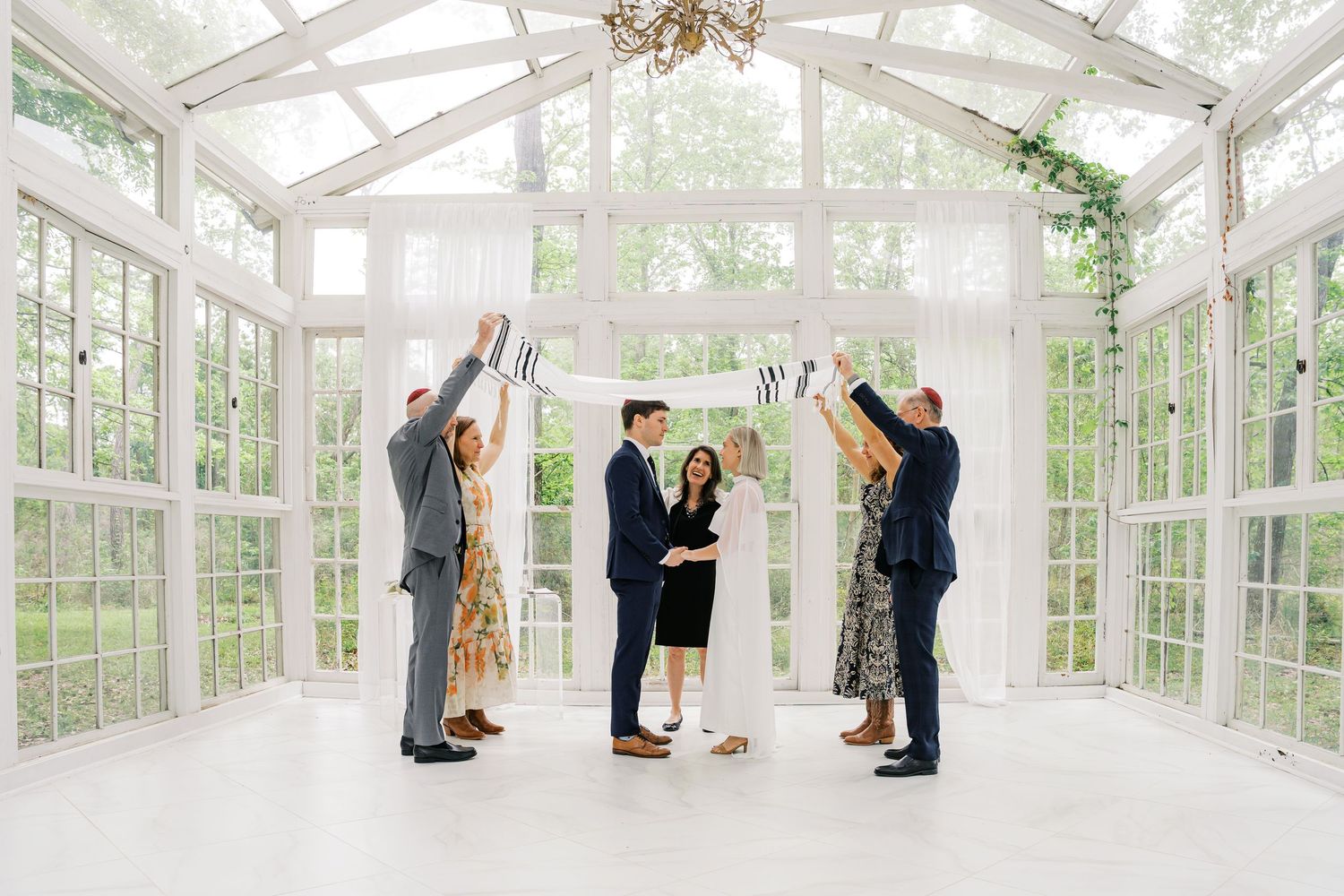 Small intimate wedding ceremony in a bright greenhouse with guests holding banner letters for the couple.