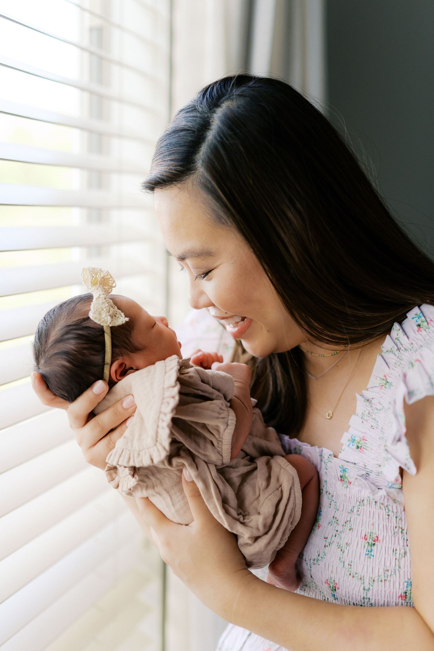 A tender moment between mother and newborn baby by a window with natural light streaming in.