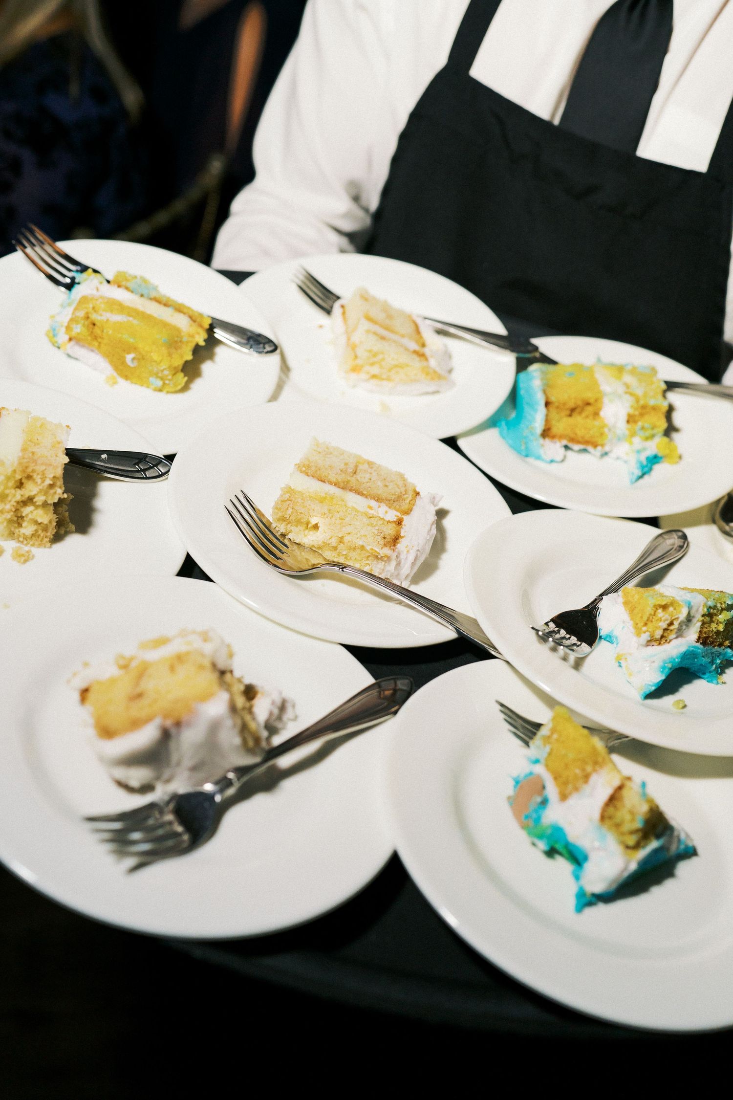 Row of white plates with partially eaten wedding cake slices on a dark surface.