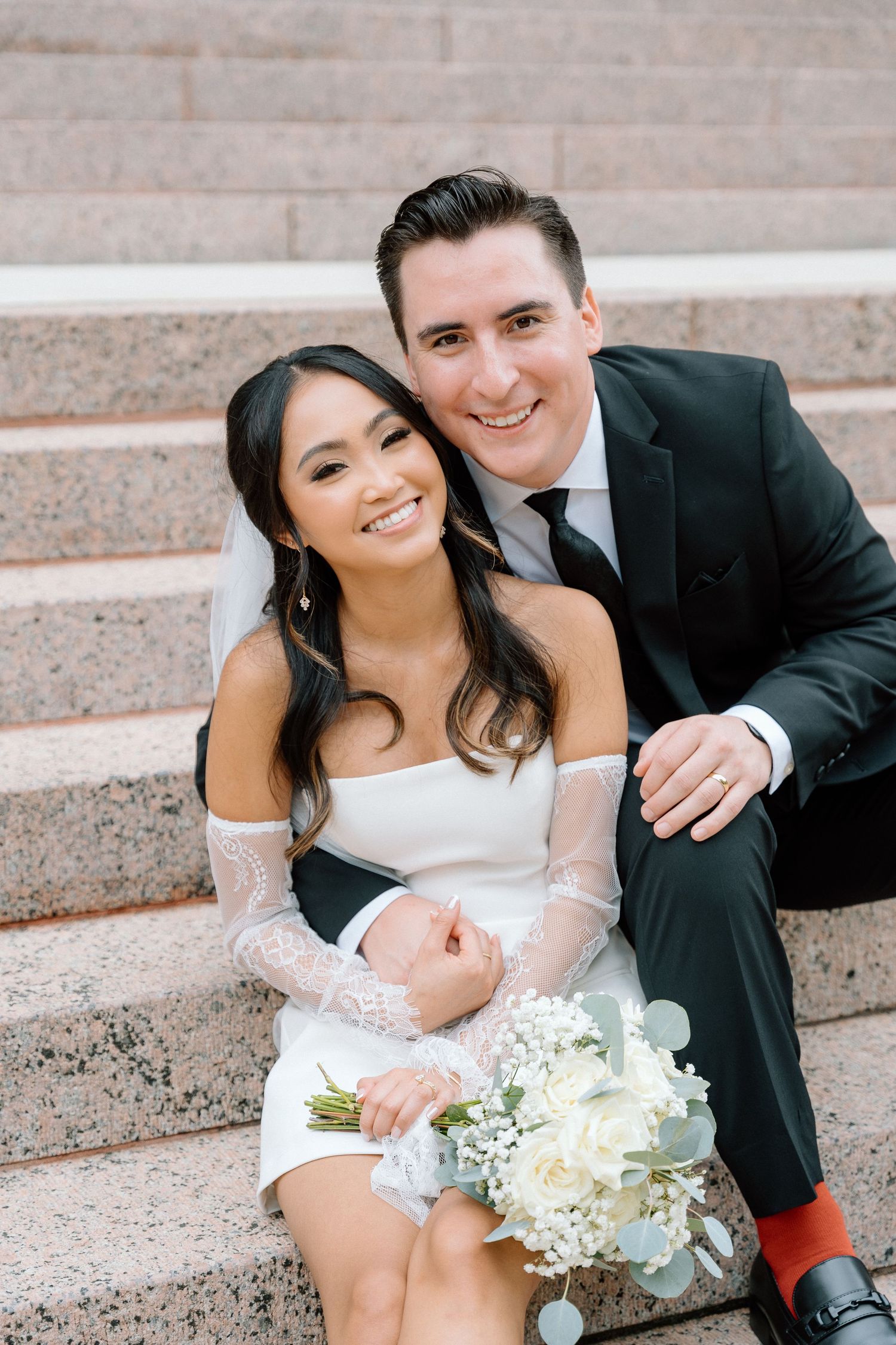 Newlyweds share intimate moment sitting on grand stone staircase.