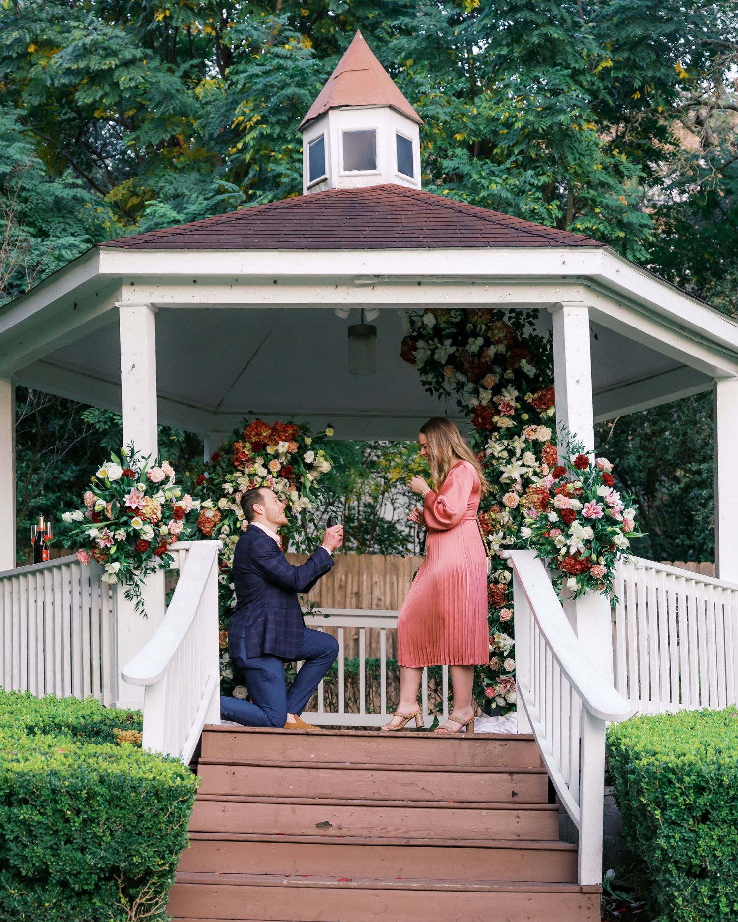 A white gazebo decorated with floral arrangements stands in a lush garden setting.