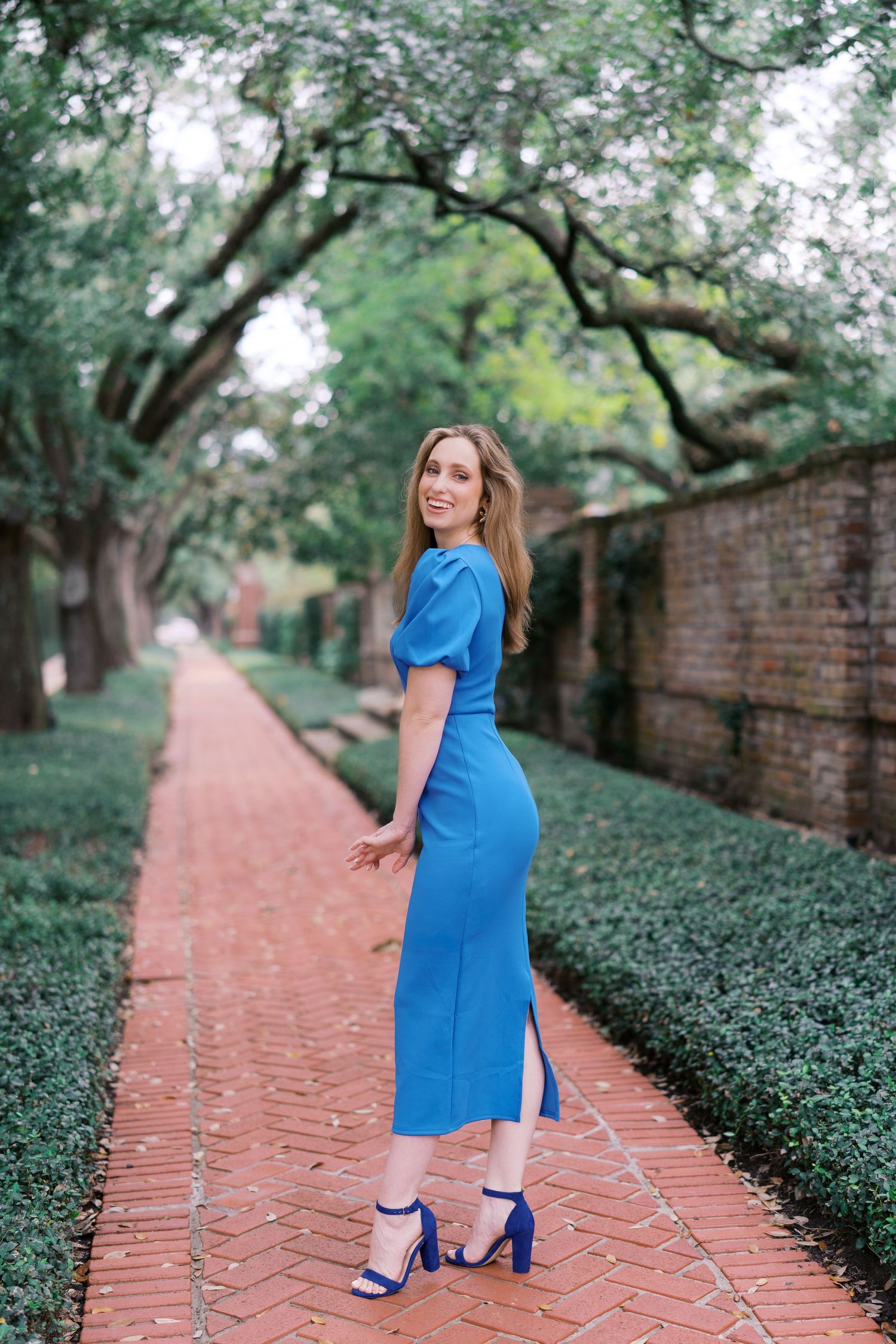 A scenic brick pathway lined with manicured hedges and trees frames a maternity photo.