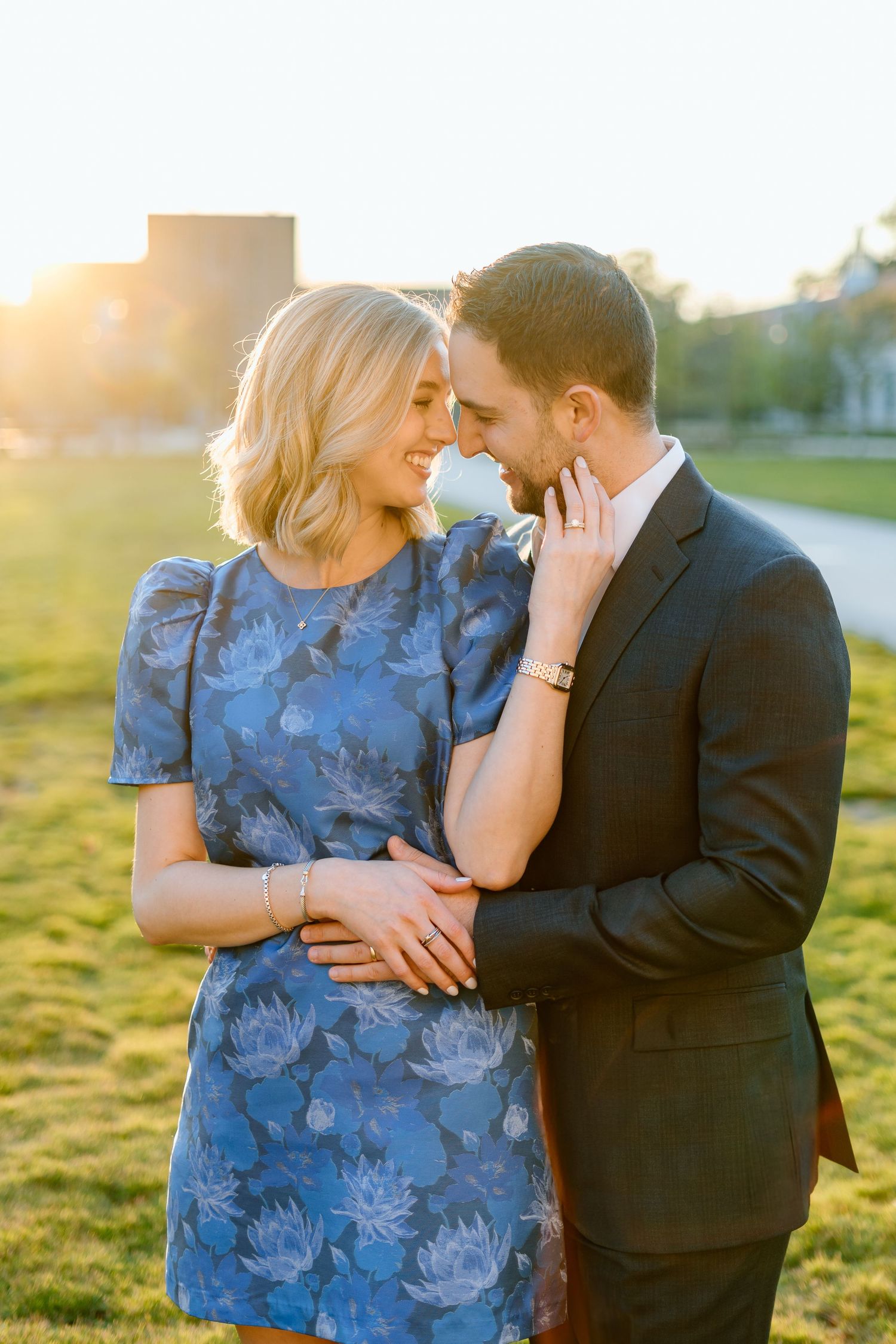 Romantic sunset portrait of couple in blue dress and suit on grassy field.