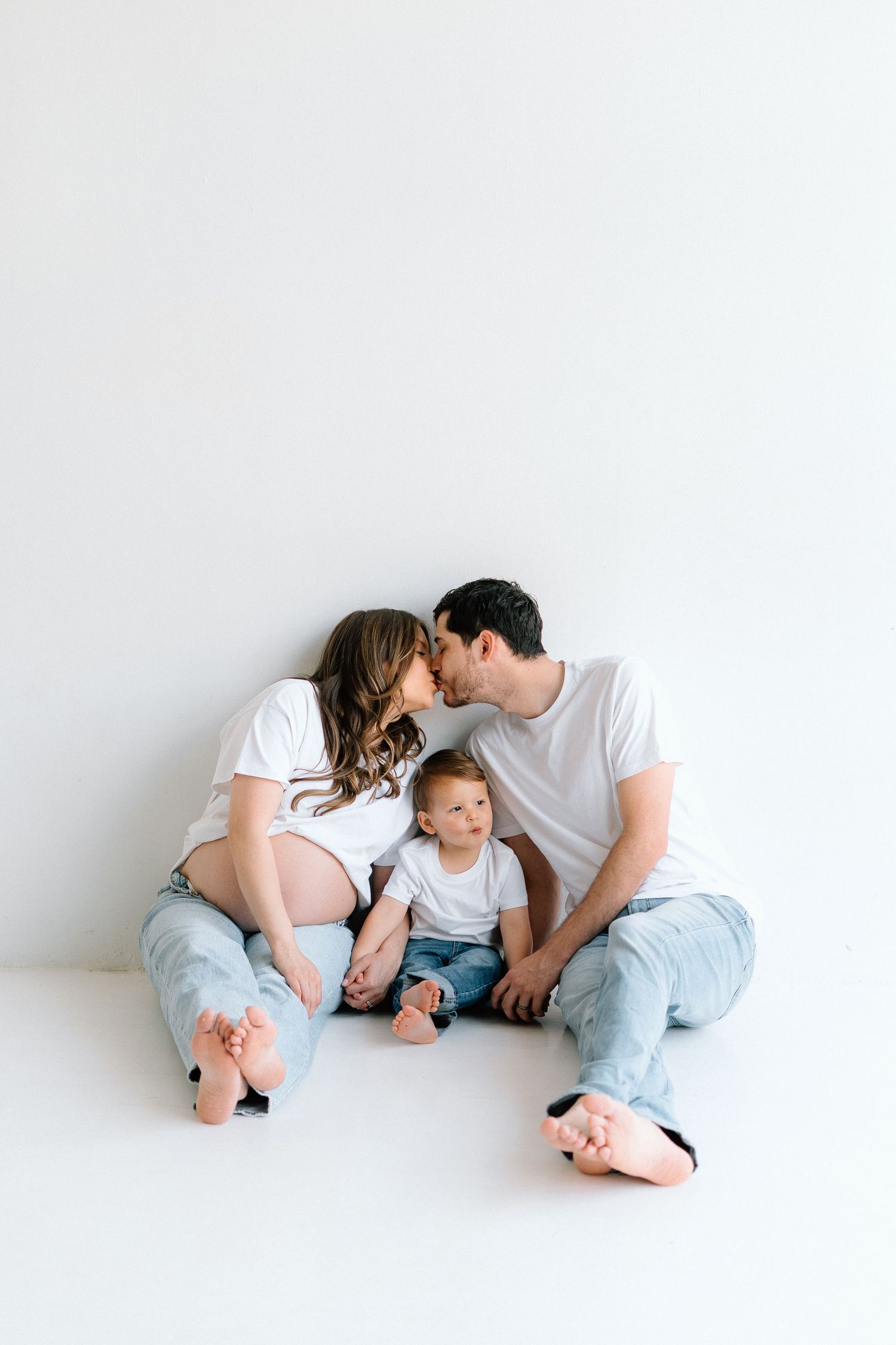 A family in matching white shirts and jeans poses together on a white background.