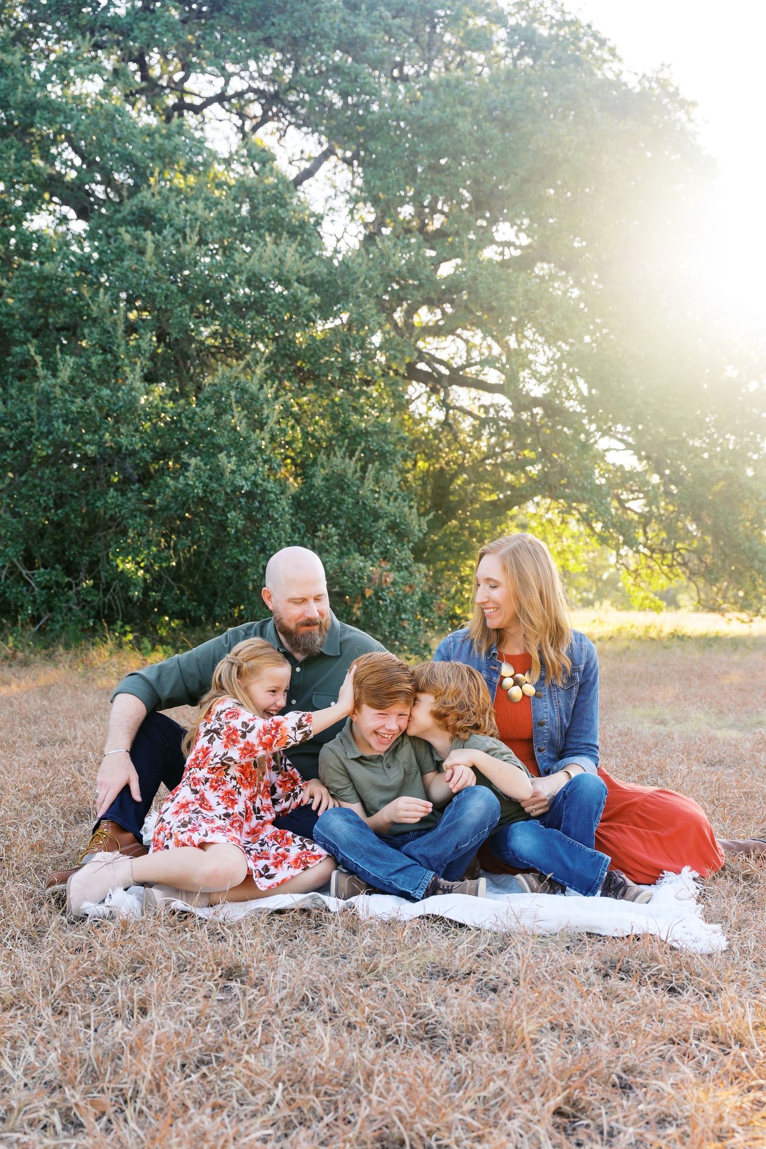 Family lying together on dry grass during golden hour sunset photography session.