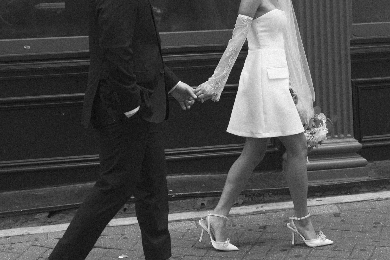 Wedding couple walking playfully on urban street with brick pavement.