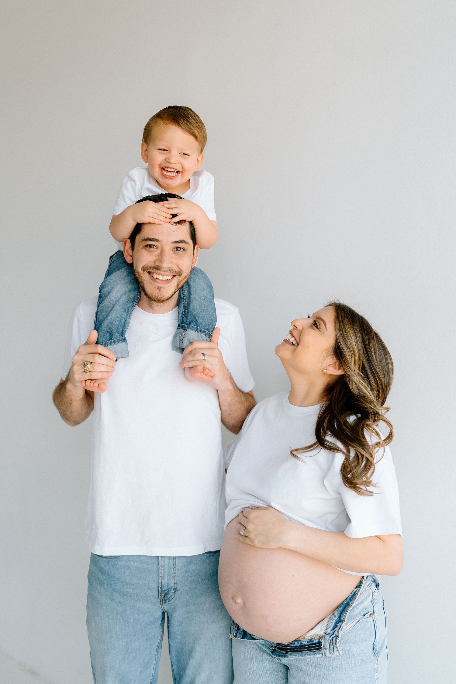 Joyful family maternity photos with playful poses and interactions in white studio setting.