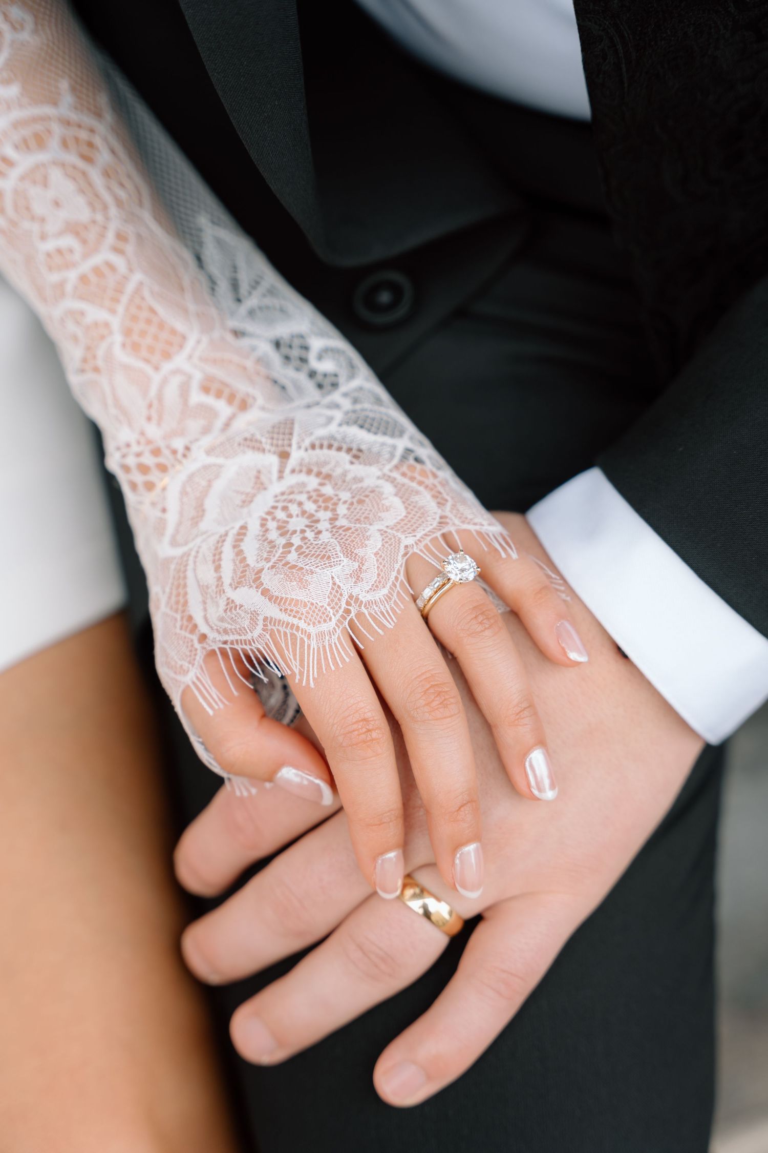 Close-up of hands with wedding rings and lace sleeve details.