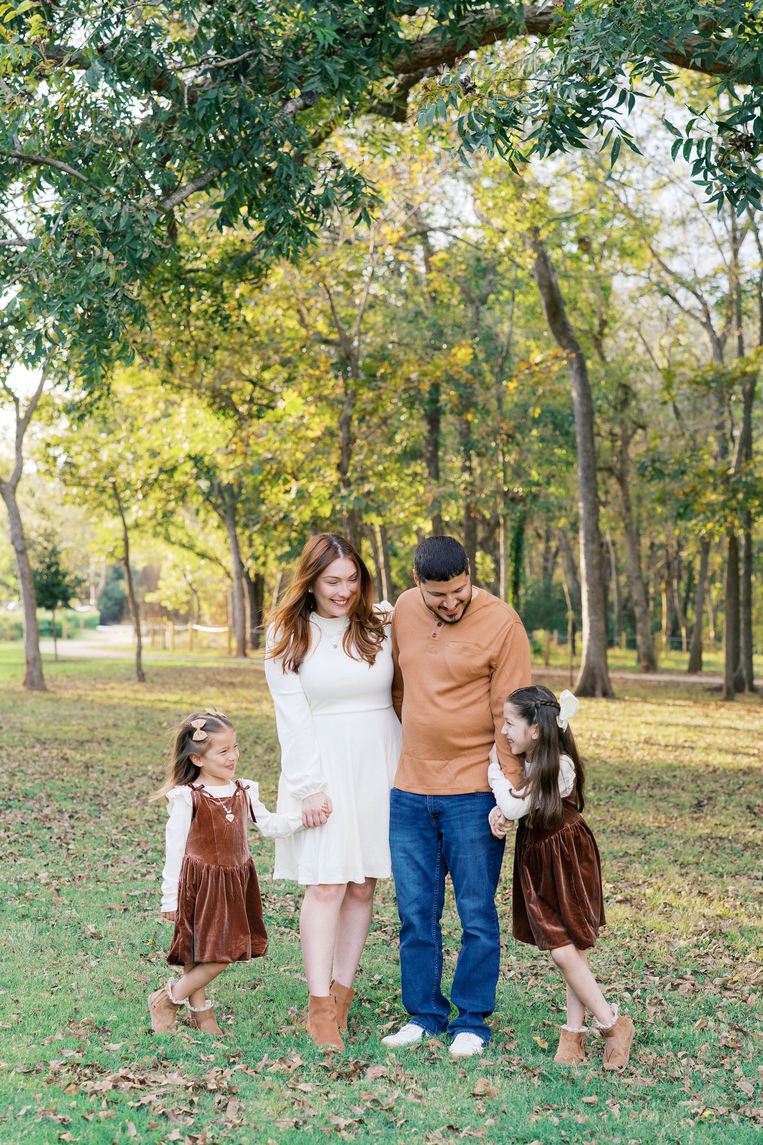 Family portrait in an autumn park with coordinated brown and white outfits among fall foliage.