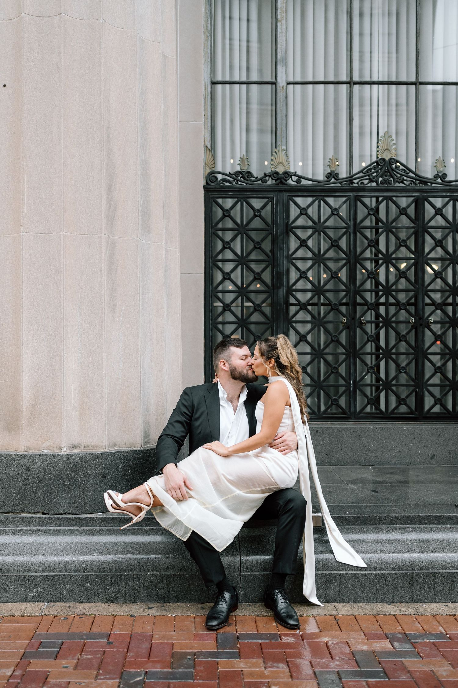 Couple shares intimate moment while sitting on architectural steps in formal wear.