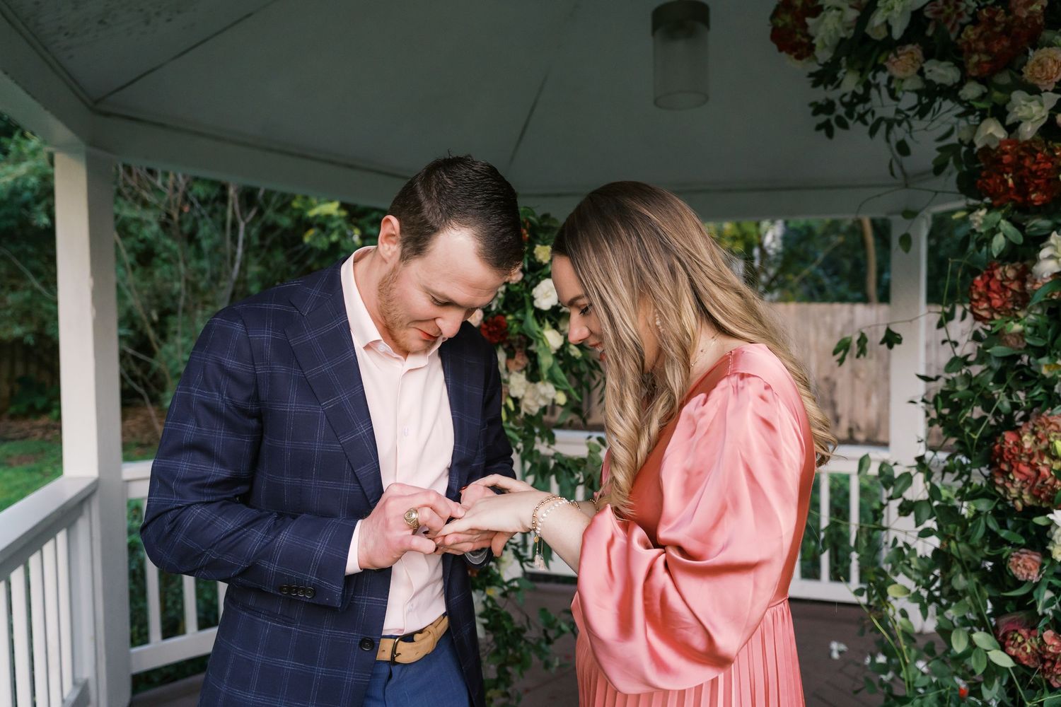 A couple shares an intimate moment on a white gazebo porch decorated with floral arrangements.