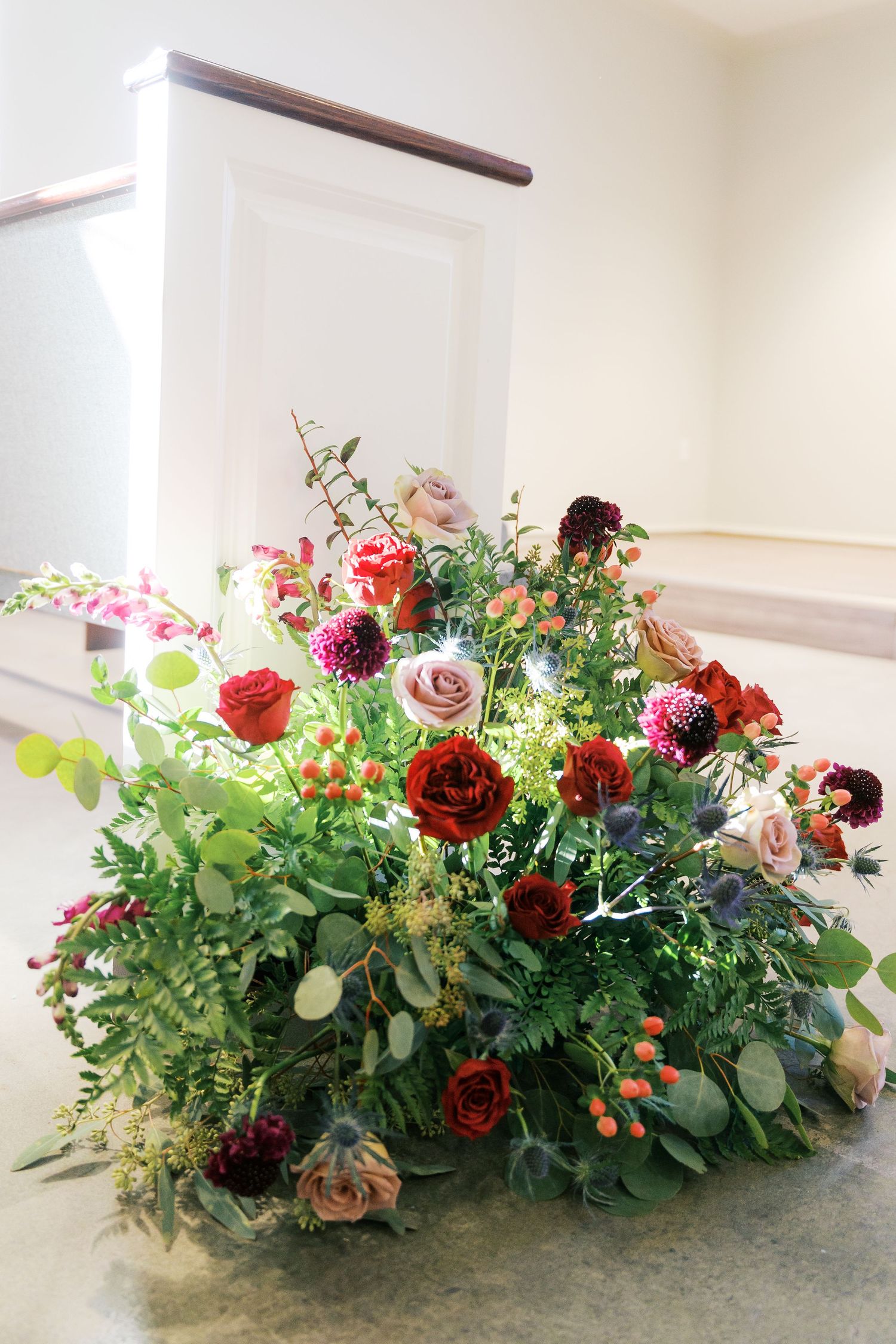 Lush floral arrangement with deep red roses and greenery displayed on a light colored surface.