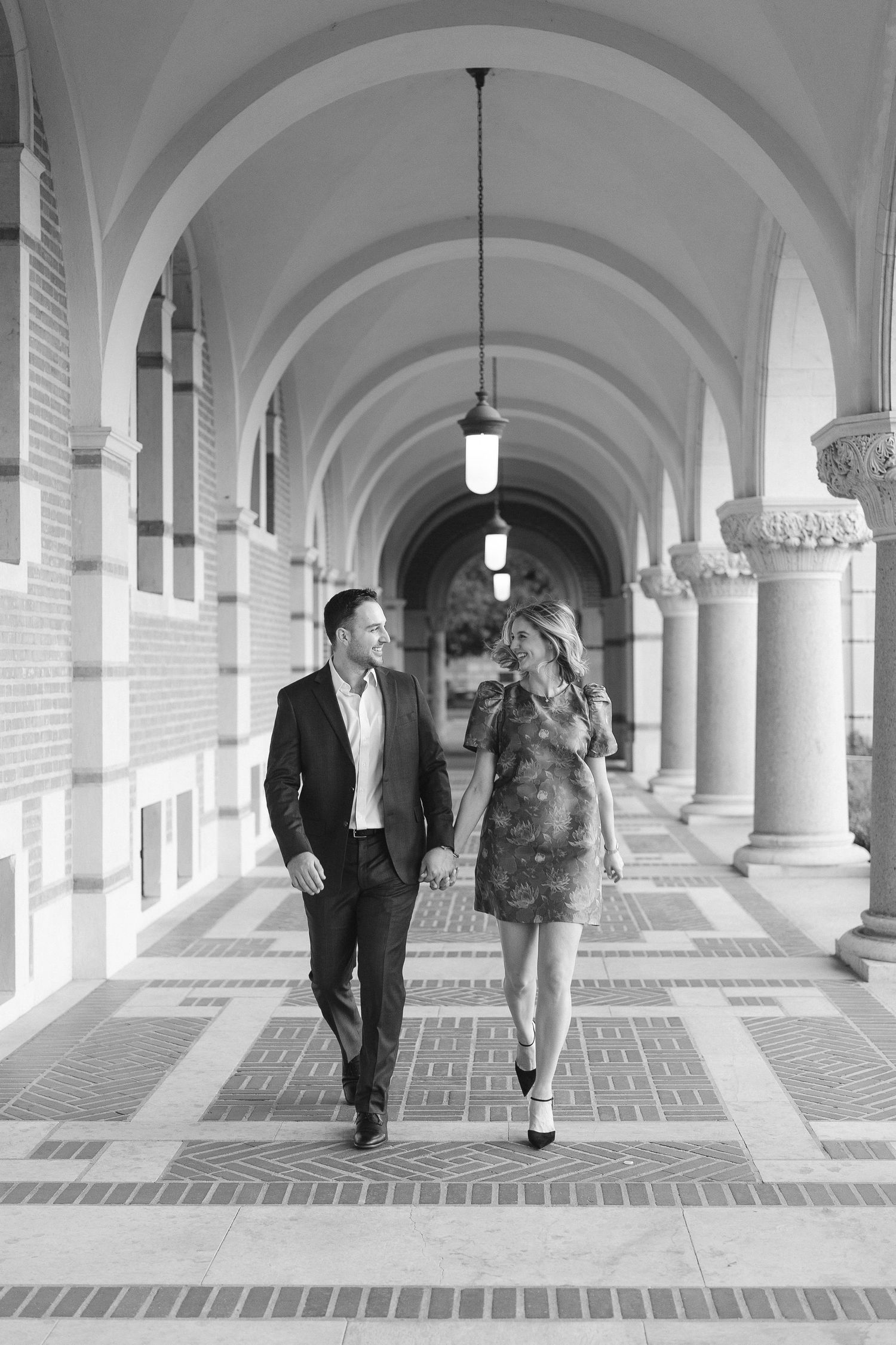 Two people walking and laughing together in an elegant arched colonnade hallway.