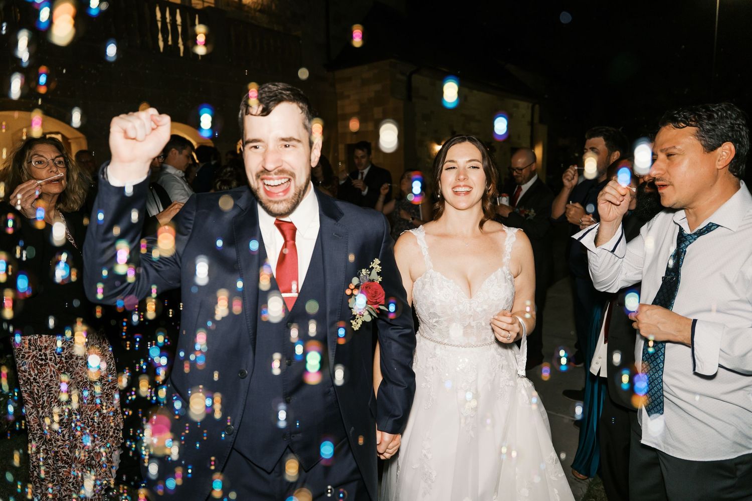 Couple celebrates during their wedding exit as guests shower them with bubbles at night.