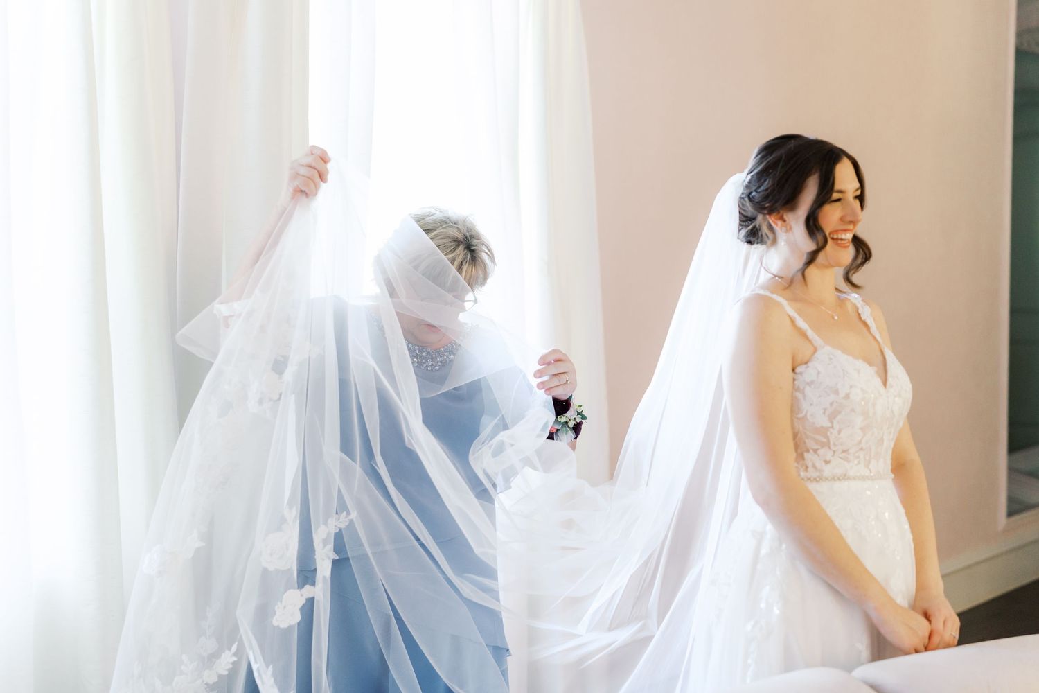A bride in white stands among flowing sheer curtains in natural light.