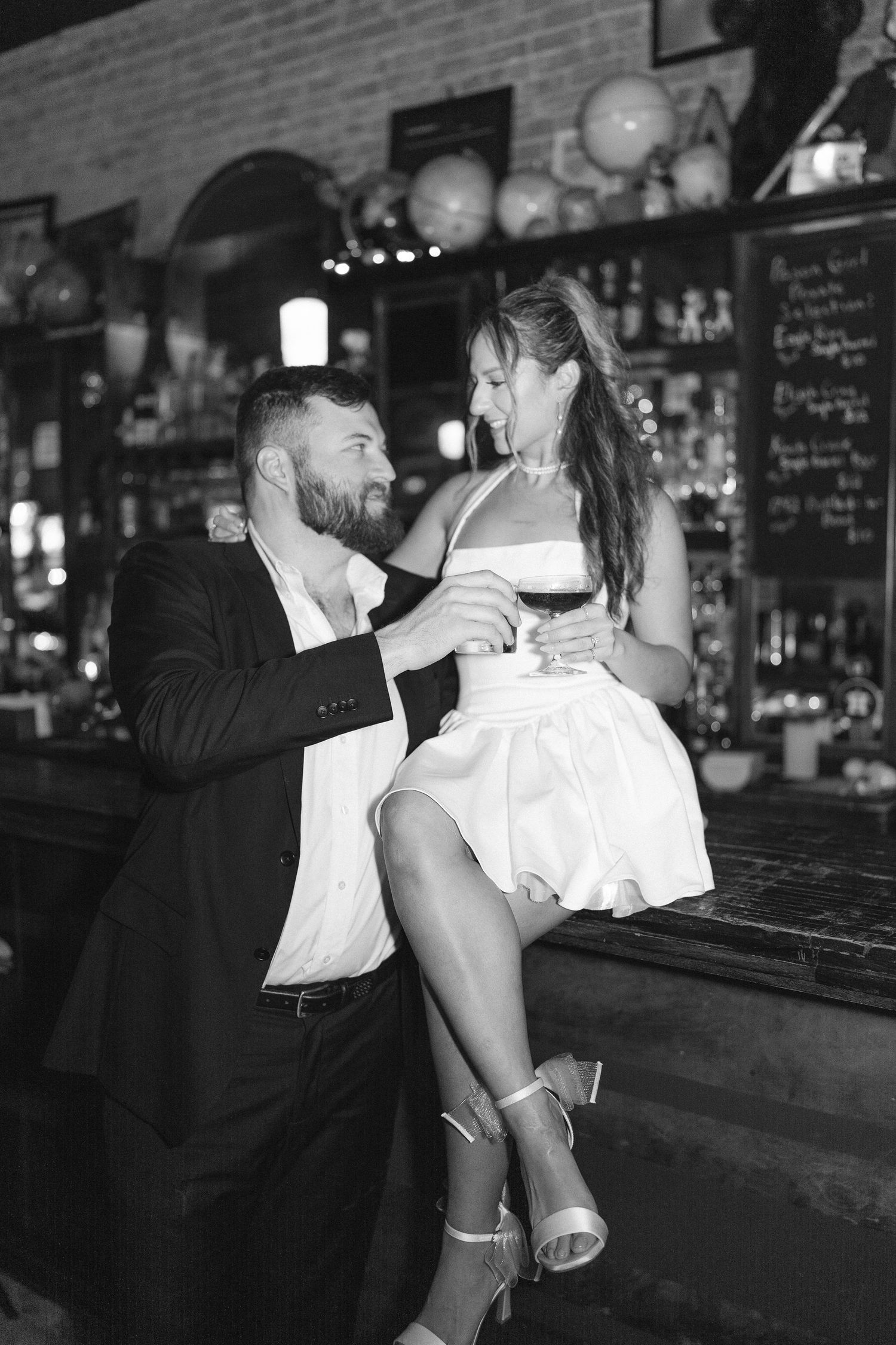 Black and white photo of couple enjoying drinks and laughter at dimly lit bar.