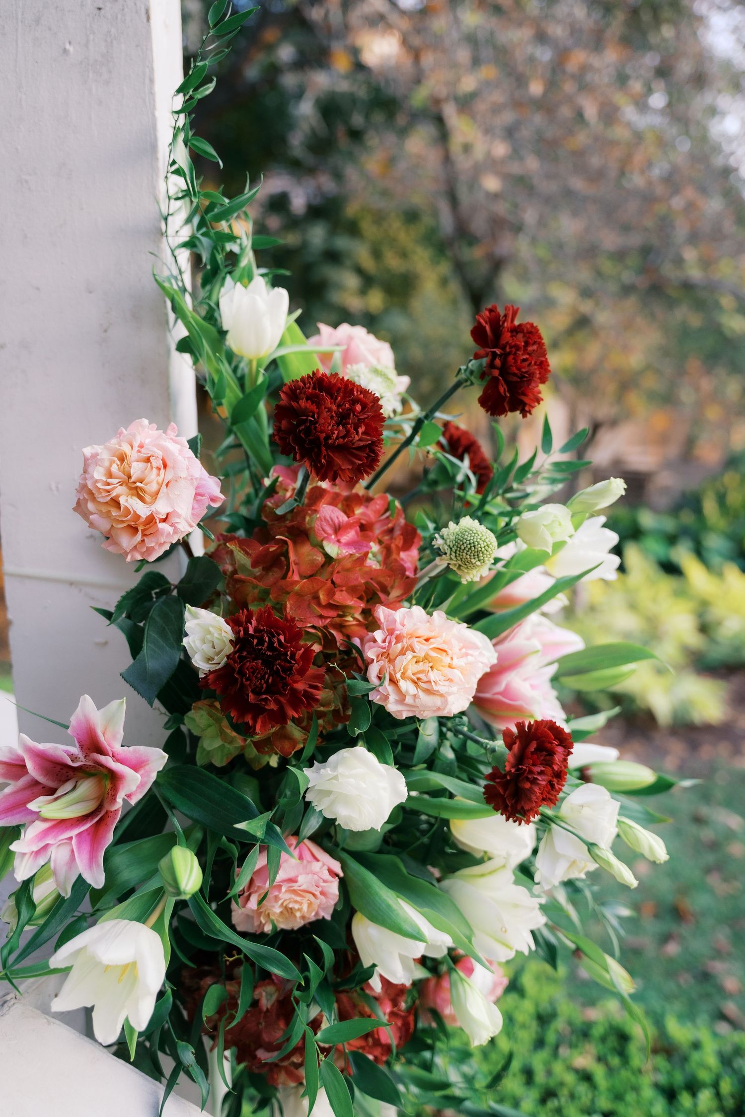 Elegant floral arrangement featuring burgundy carnations, pink lilies, and peach roses against greenery.