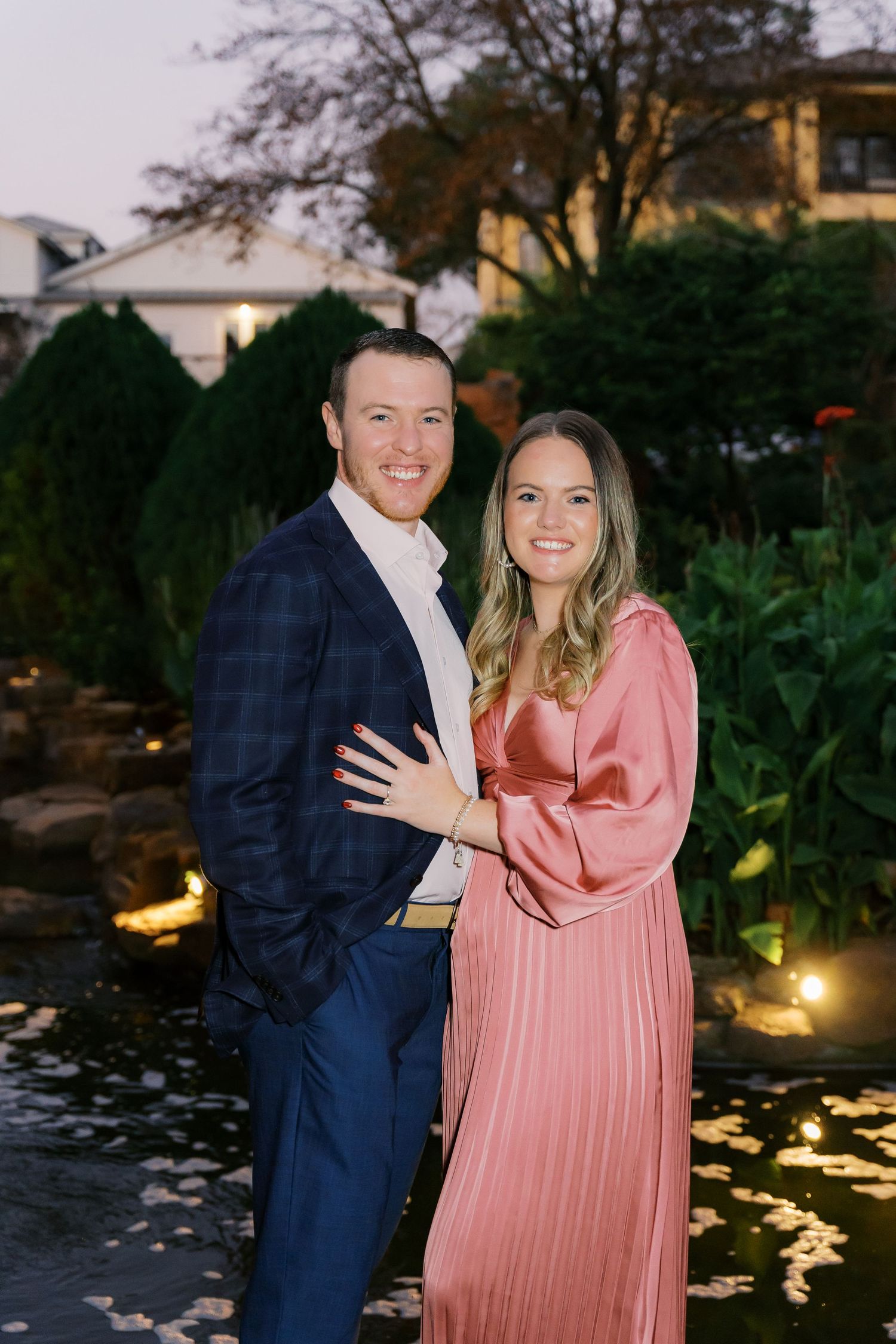 Engagement announcement photos taken in a garden setting with decorative lighting.