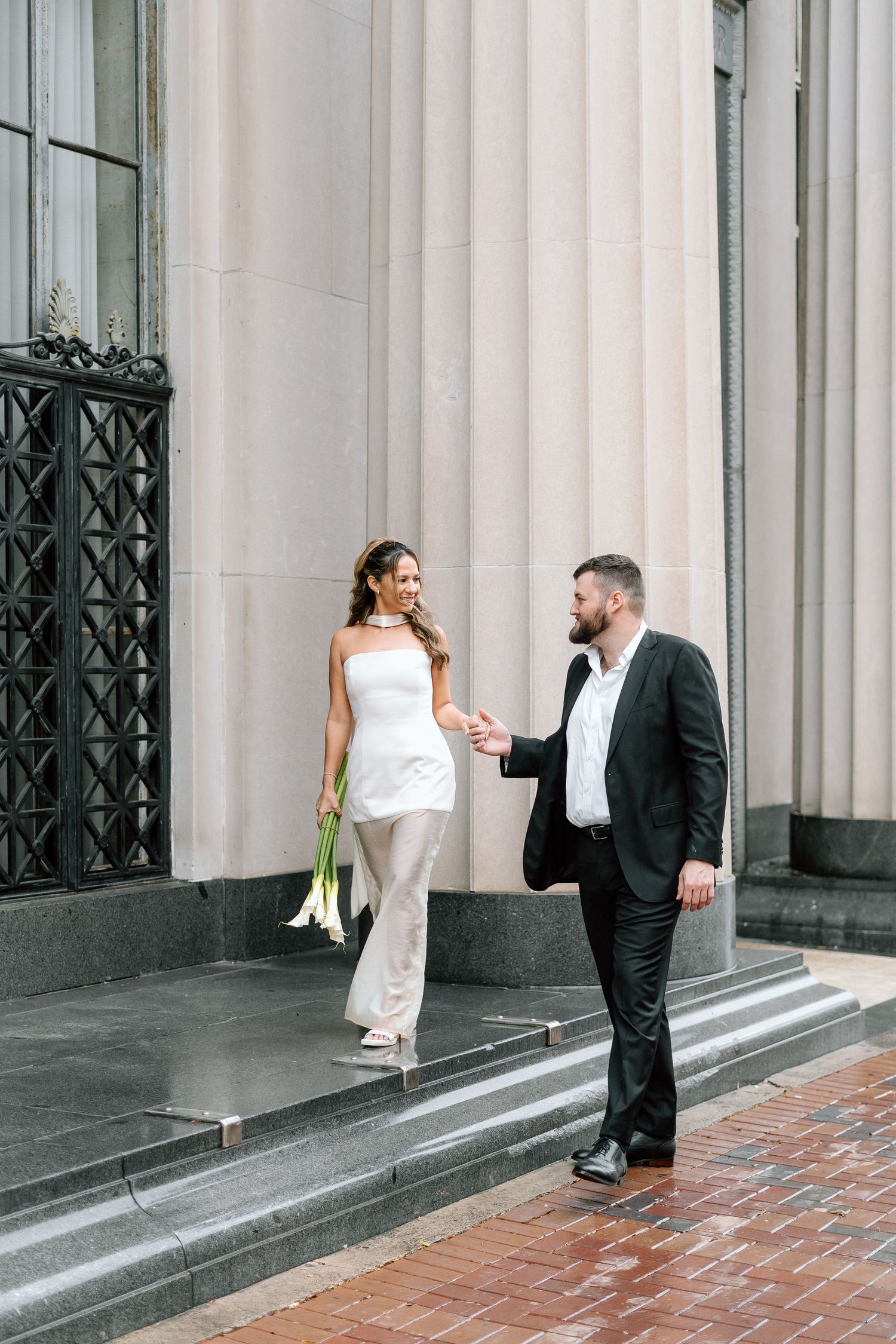 Romantic couple poses playfully on stone steps of historic building in formal attire.