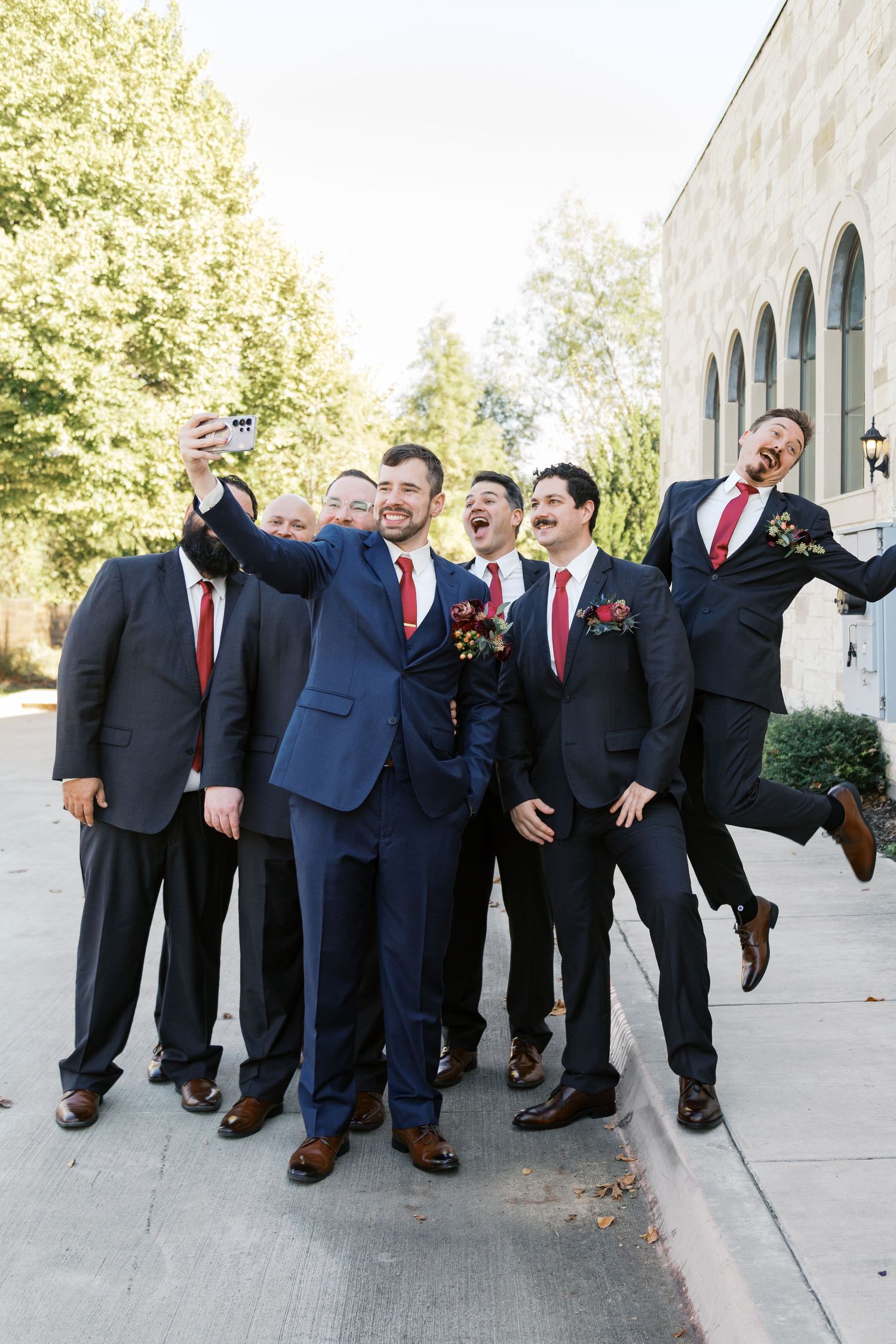 Groomsmen in navy and black suits taking fun selfie photo outside venue.