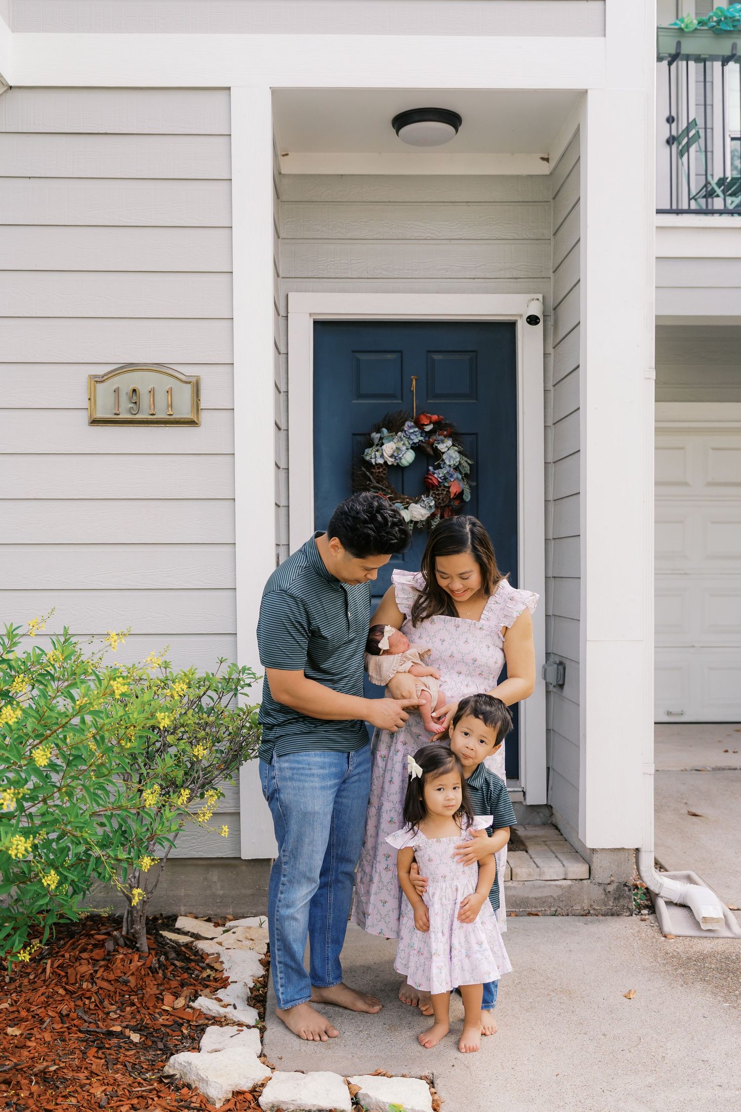 Family shares tender moment together on porch of white house with blue door.
