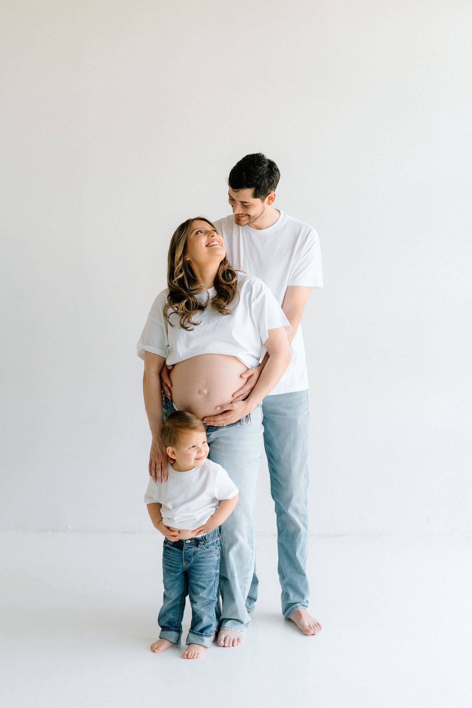 A family poses together against a white backdrop showing affection and anticipation of a new baby.