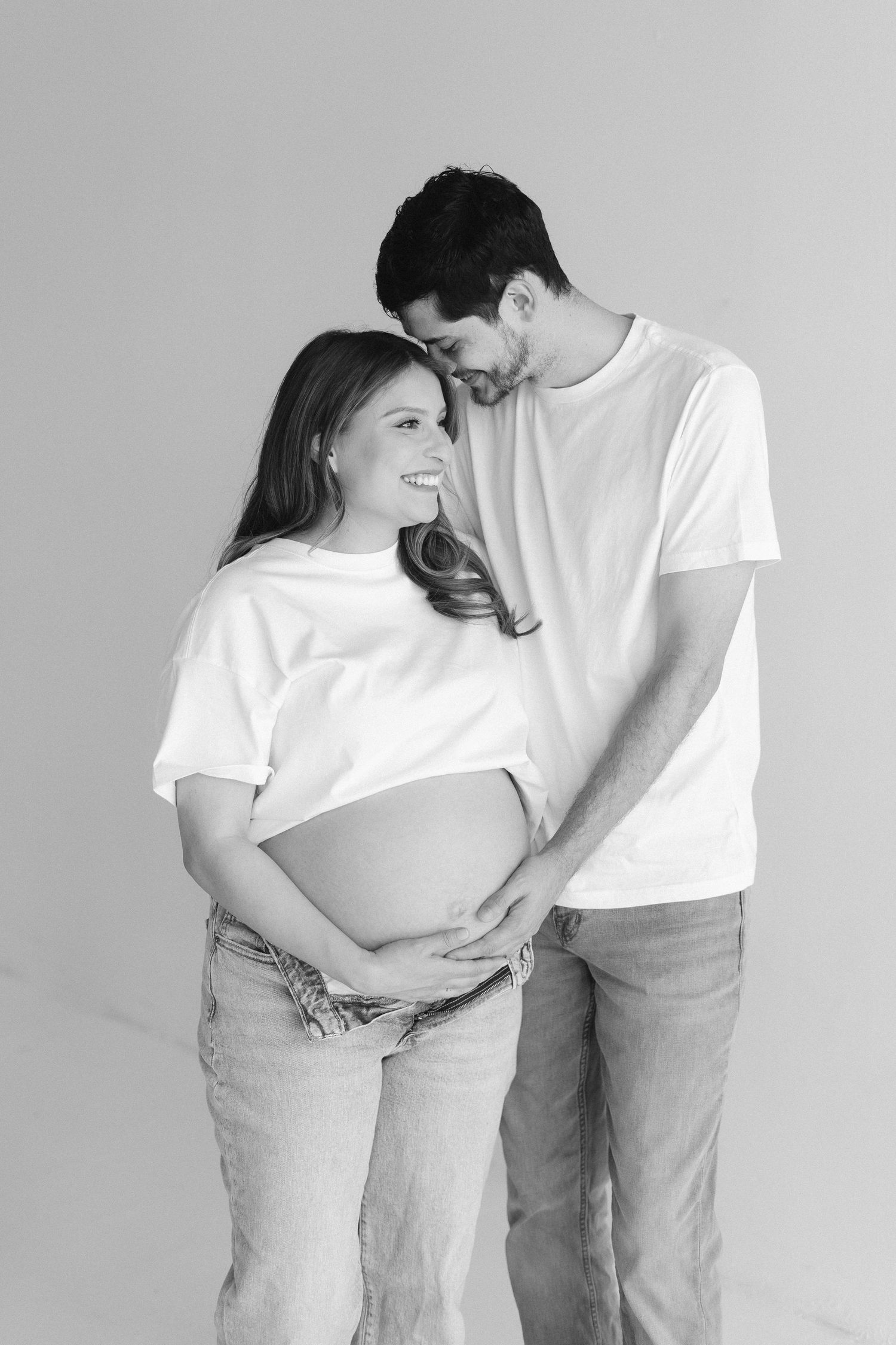 Intimate black and white photo series showing a couple in white shirts and jeans embracing against a plain wall.