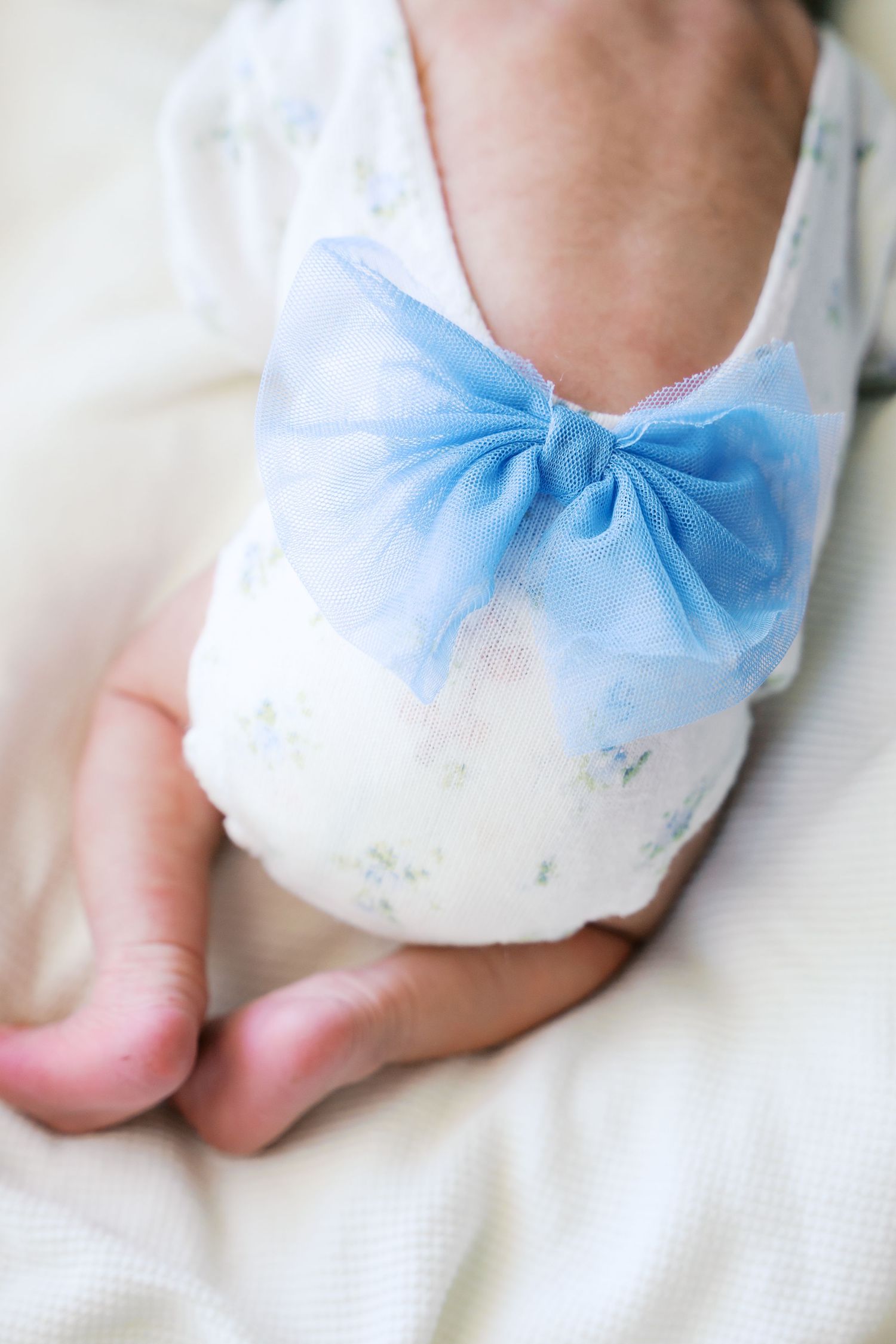 White baby shoes adorned with delicate light blue bows against a soft white background.