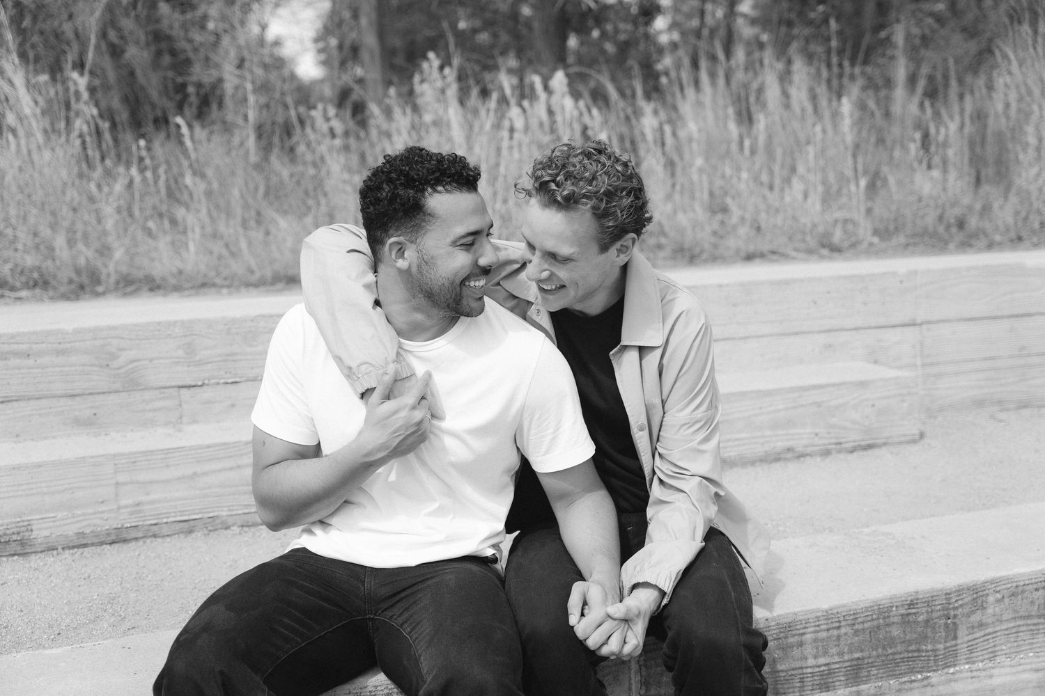 A romantic black and white photo of a couple sitting close together and sharing a tender moment on a bench outdoors.